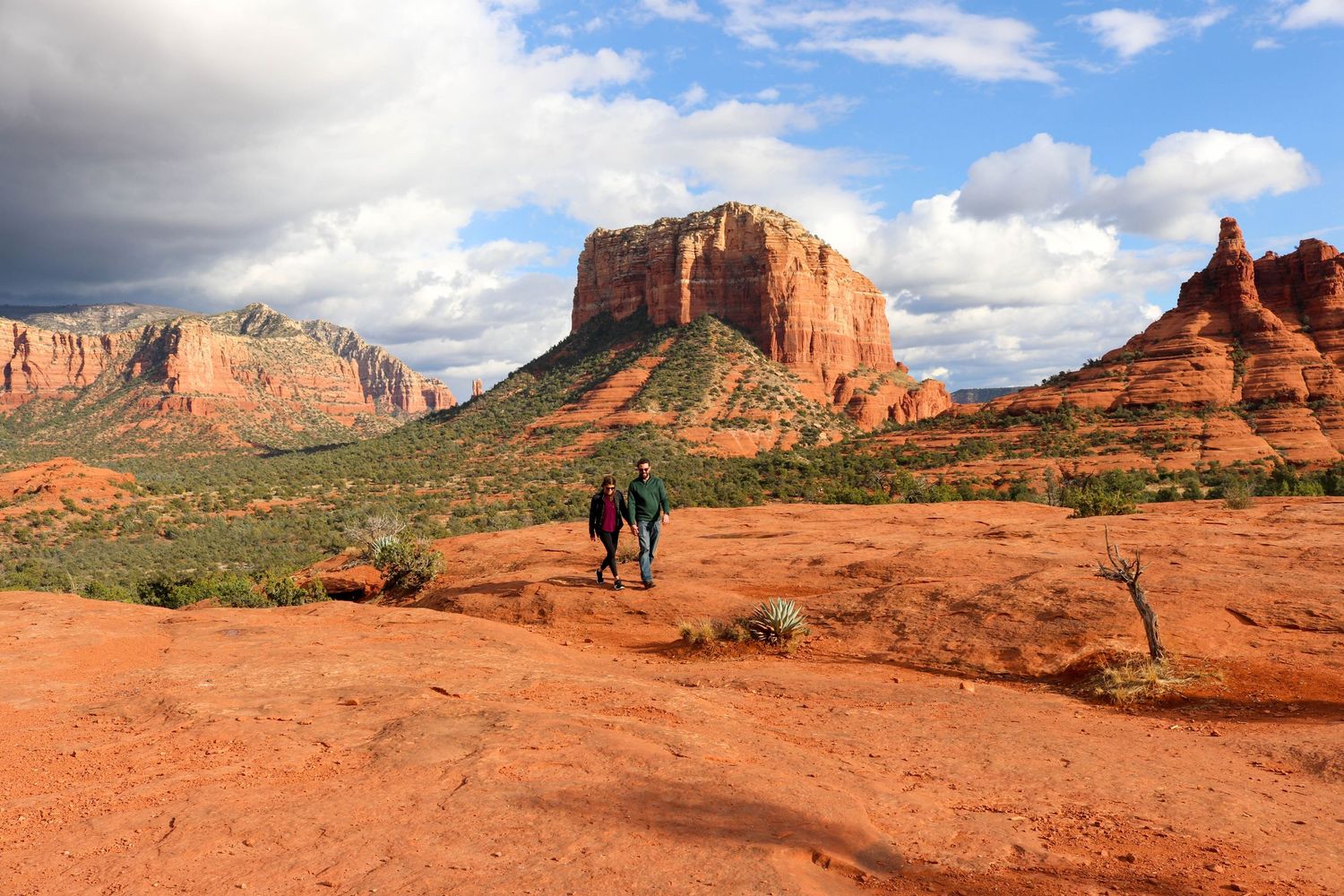 Panoramic view of red rock formations and desert landscape in Sedona, Arizona under cloudy blue skies.