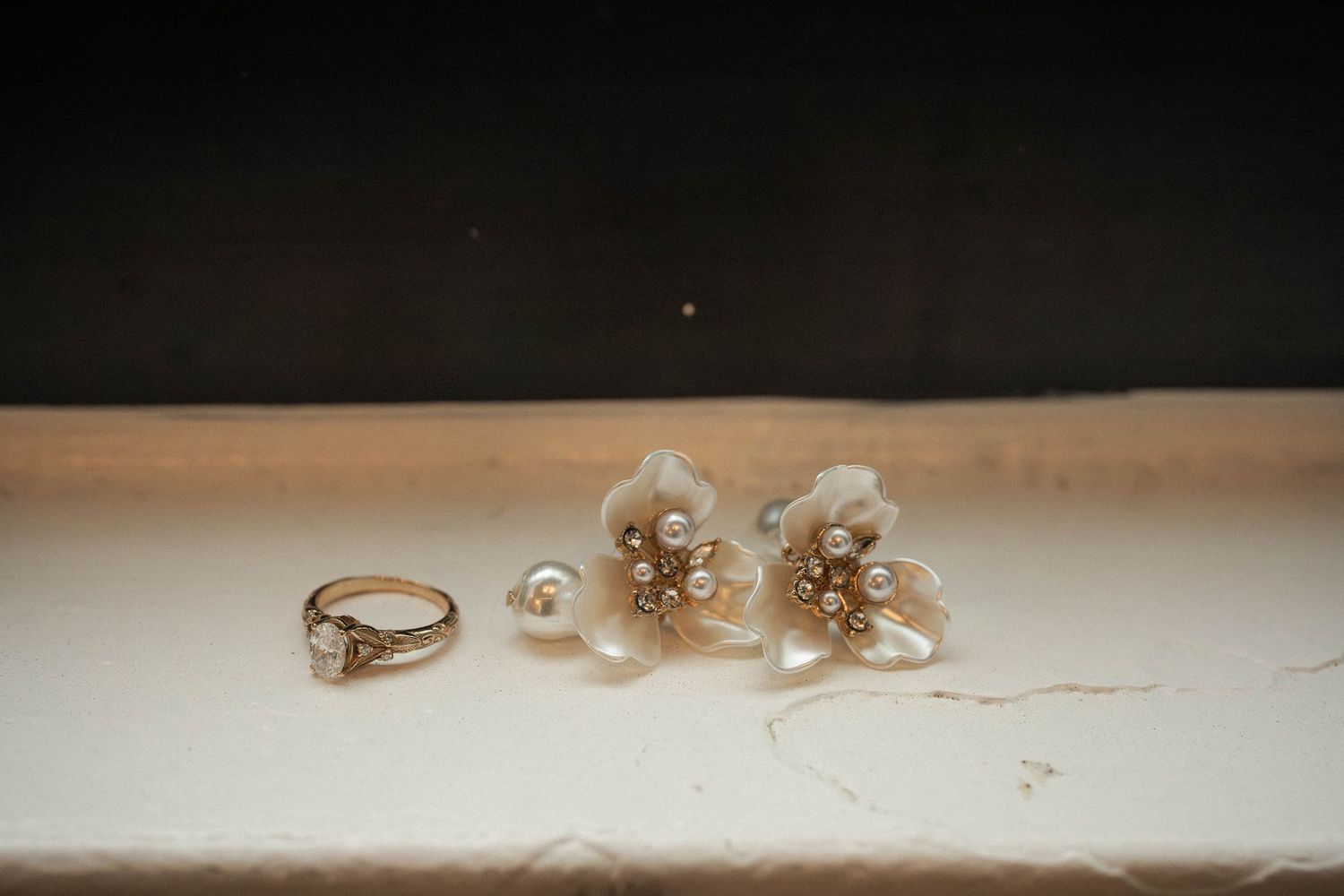 Delicate pearl flower earrings and a gold diamond ring displayed on a white surface for a bridal jewelry flat lay.