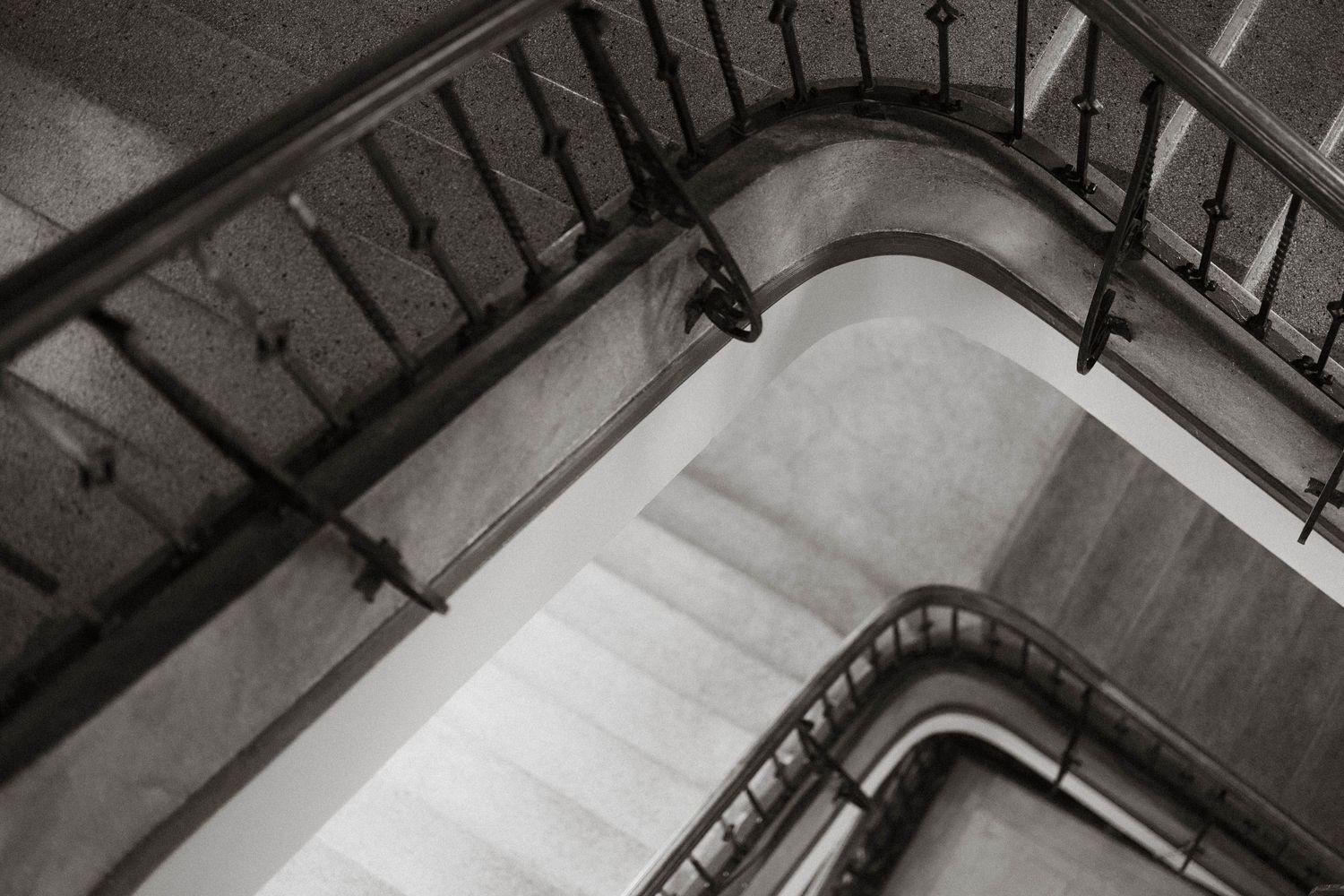 Black and white aerial view of elegant spiral staircase with ornate iron railings in classic architecture.