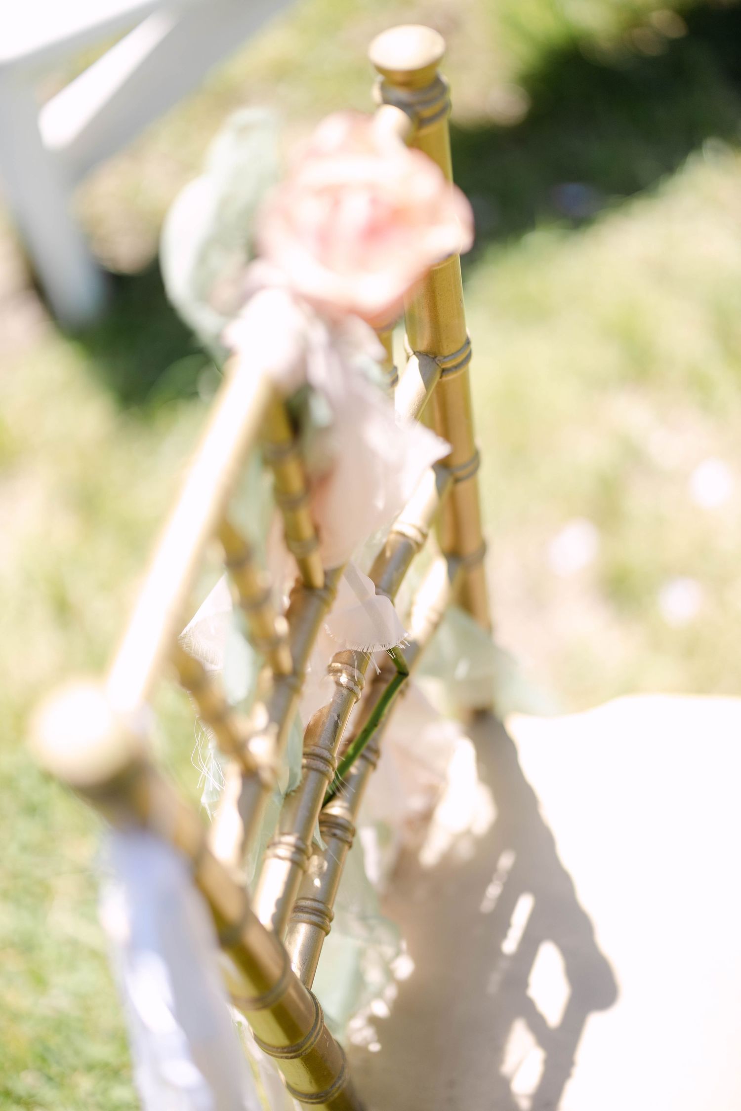 Gold chiavari chair decorated with blush pink roses and ribbons at outdoor wedding ceremony.