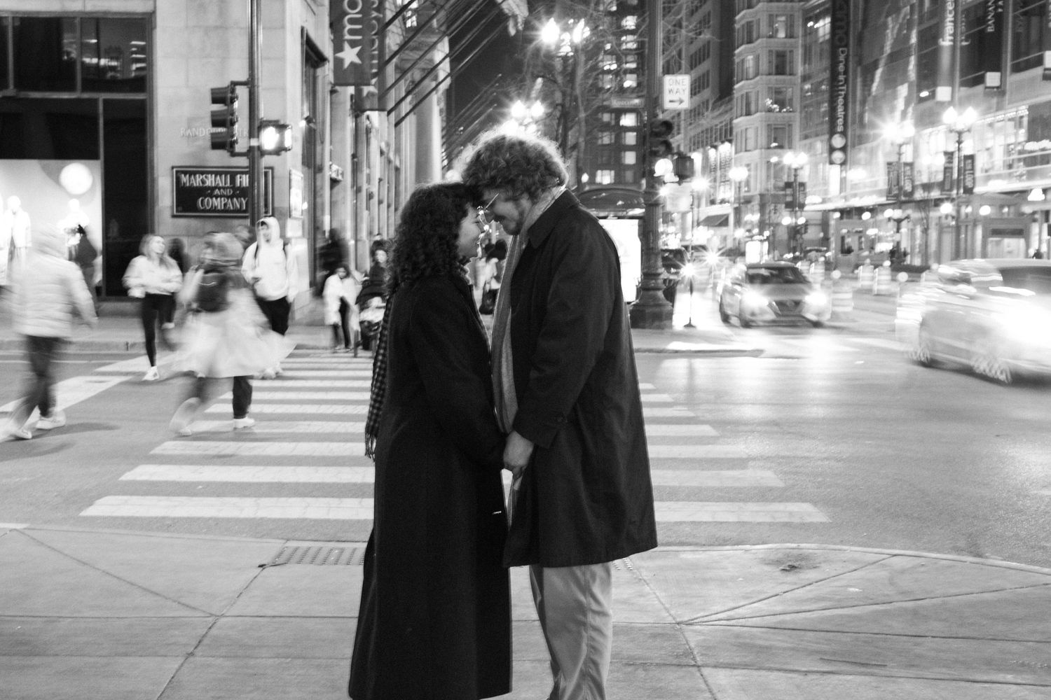 Black and white photo of a romantic couple almost kissing on a busy city street at night.