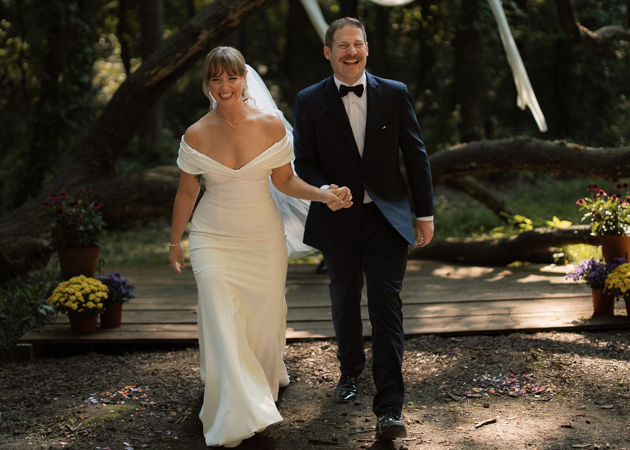 A couple in wedding attire walks together along a sunlit garden path during an outdoor ceremony.