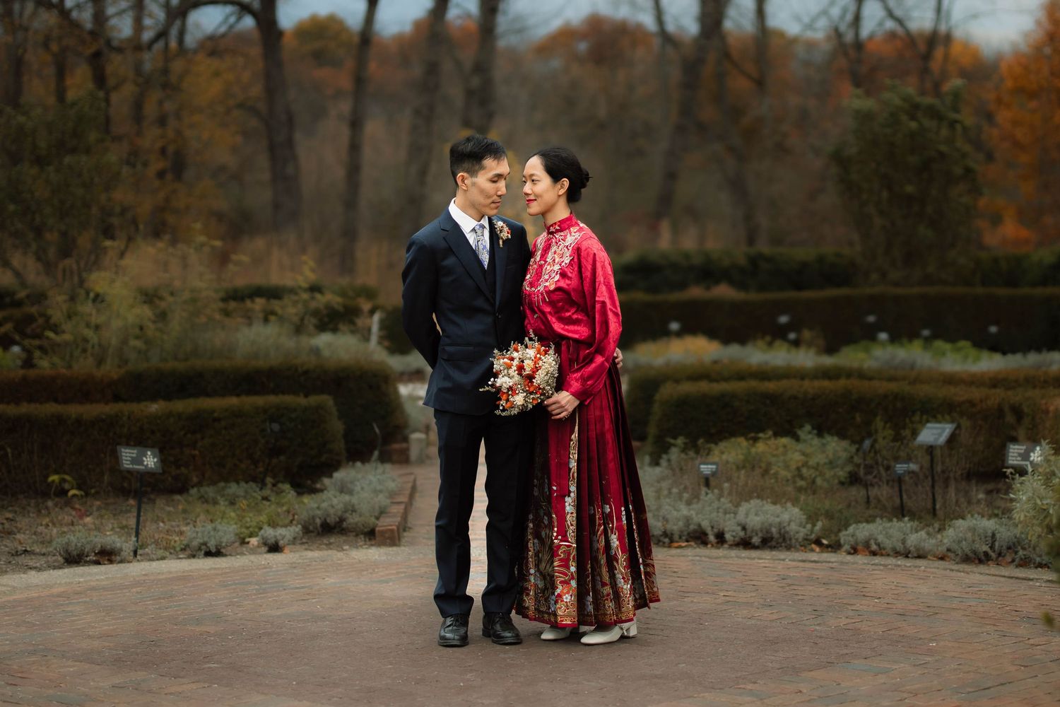 Autumn wedding scene with couple in formal attire and red dress.