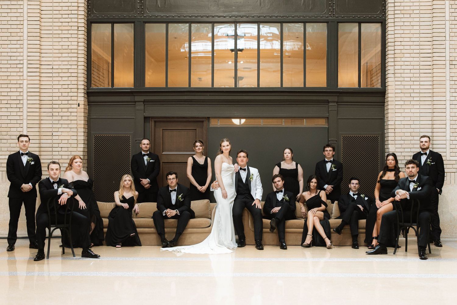 Wedding party in black and white formal attire posing together in a grand elegant venue interior.