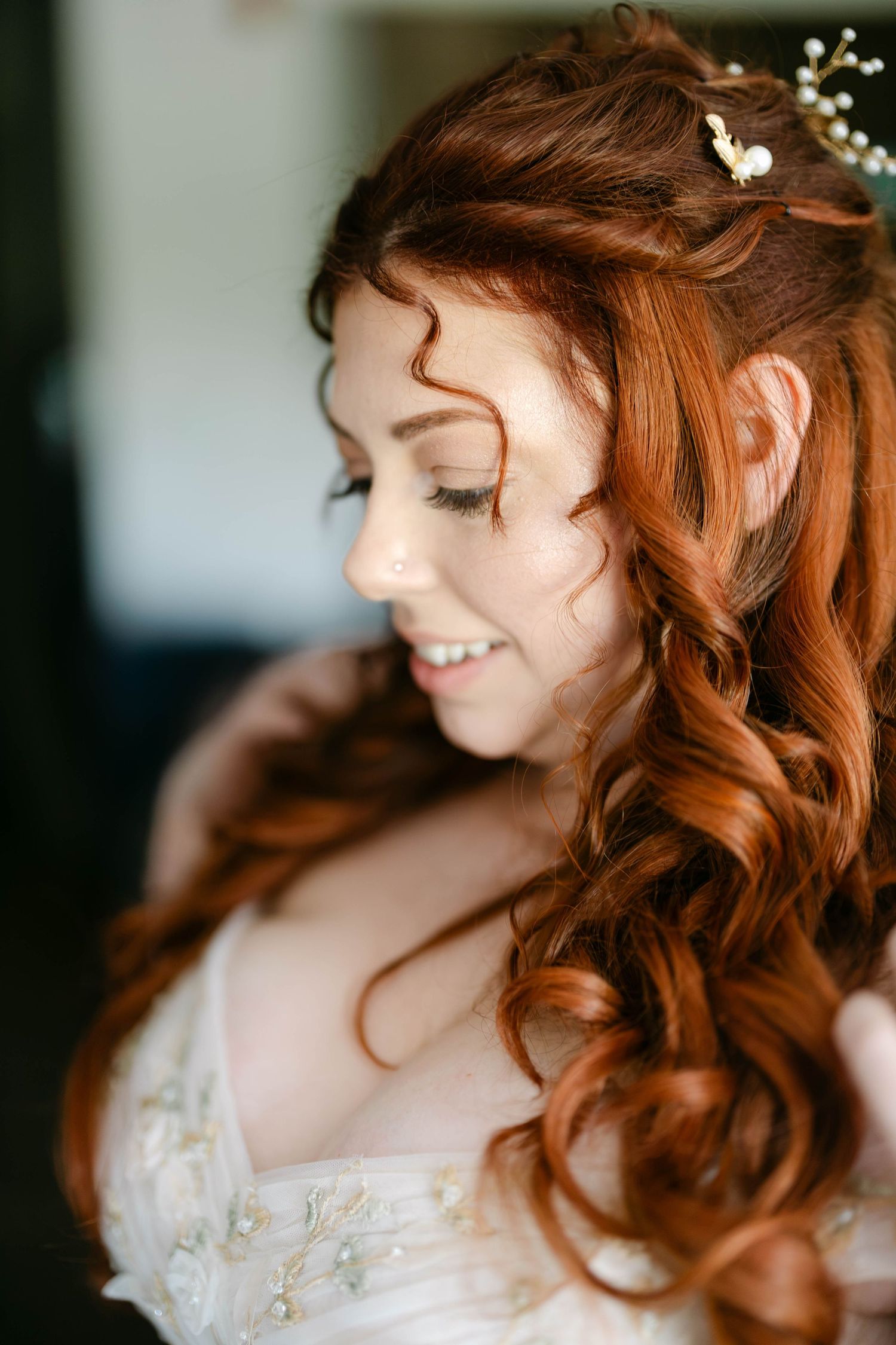 Close-up of bride with curly red hair adorned with floral hairpiece on her wedding day.