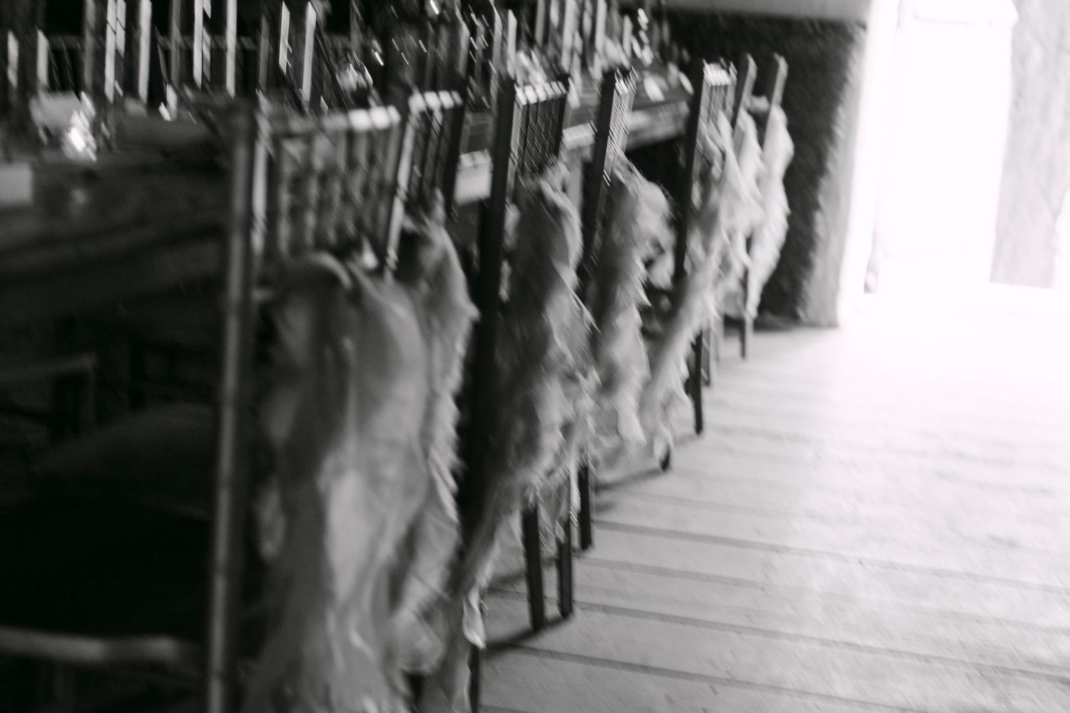 Blurry black and white photo of wedding dresses hanging on racks inside a venue corridor.