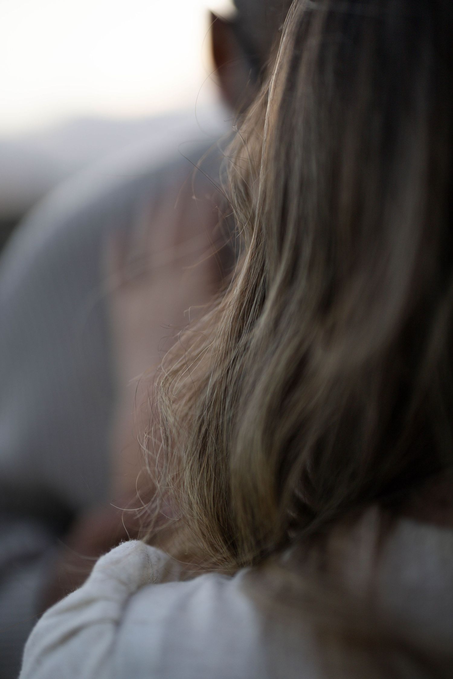 Close-up rear view of a woman with long blonde hair wearing a white top outdoors.