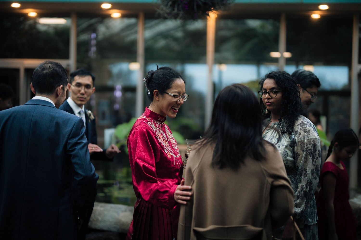 Guests in formal attire socializing at an evening event, woman in red dress laughing with friends.
