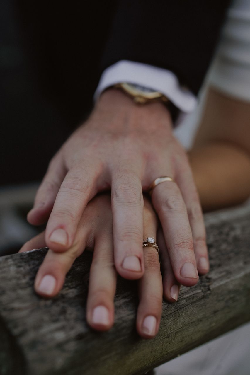 Close-up of newlywed couple's hands resting on wooden railing, showcasing wedding rings.