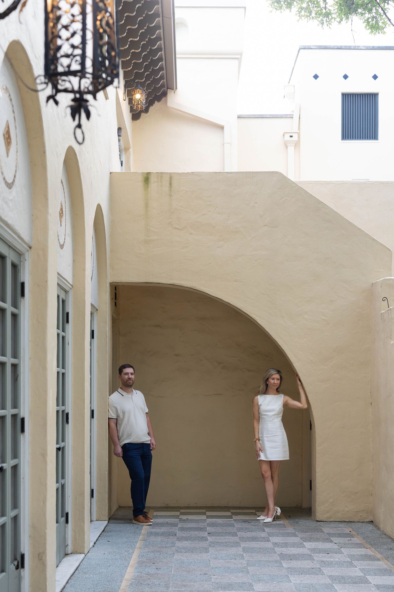 Couple posing separately under arched alcove of elegant cream-colored building.