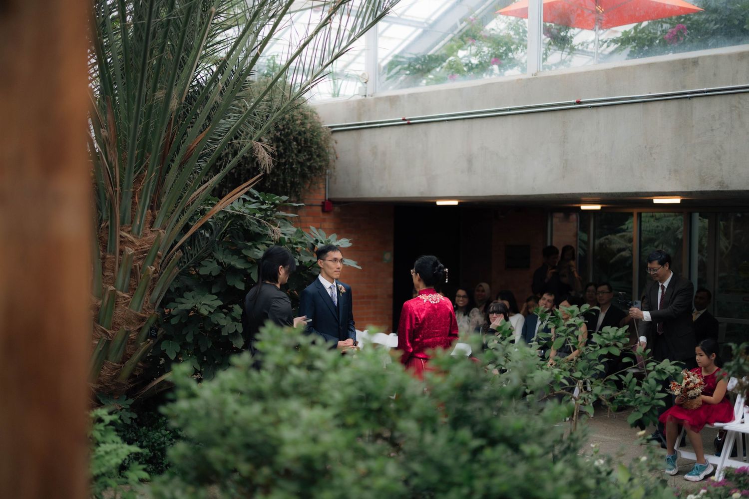Guests mingle in a lush indoor garden courtyard during an elegant wedding ceremony.