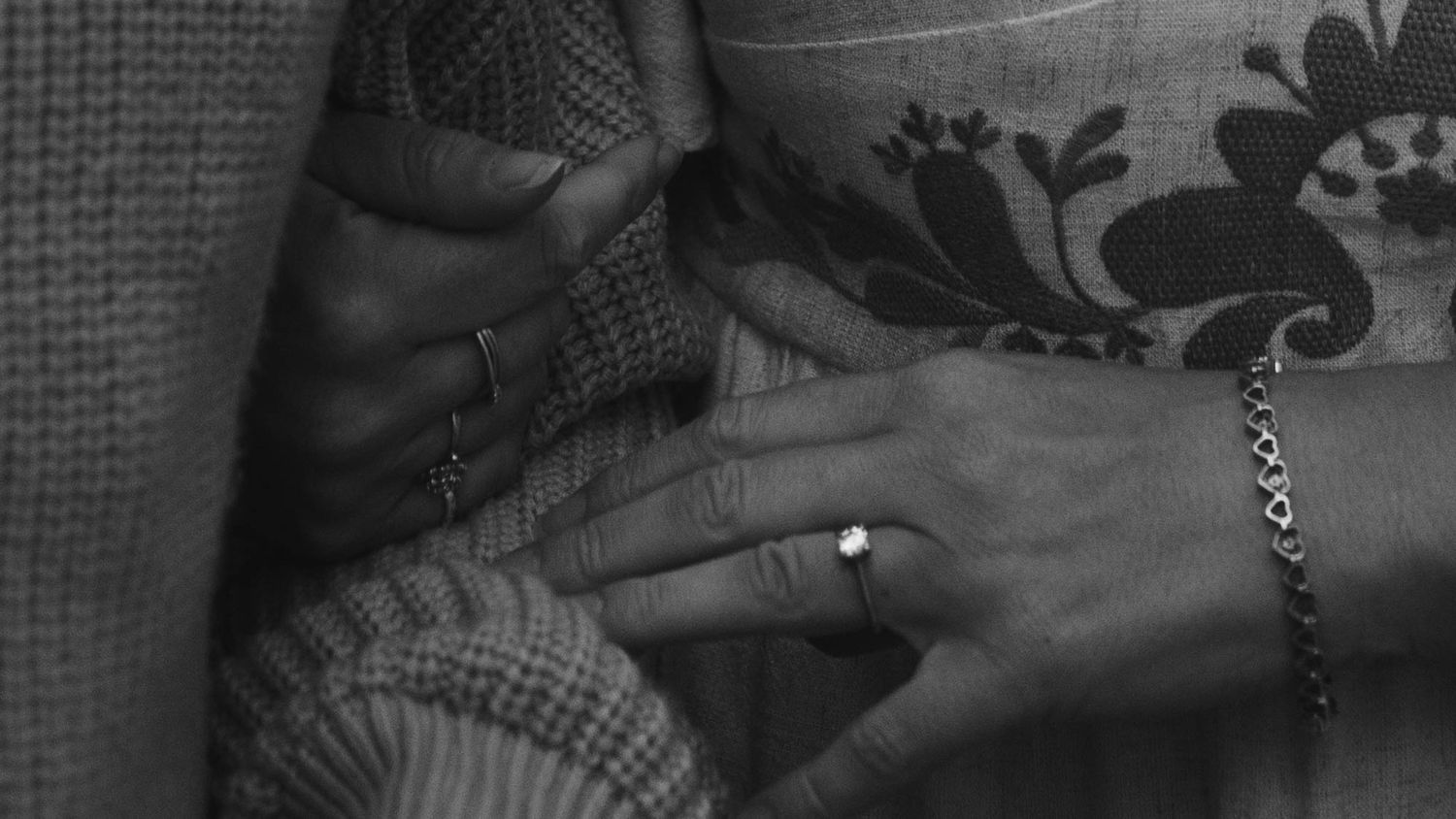 Close-up black and white photo of two hands touching, one wearing a diamond ring and bracelet.