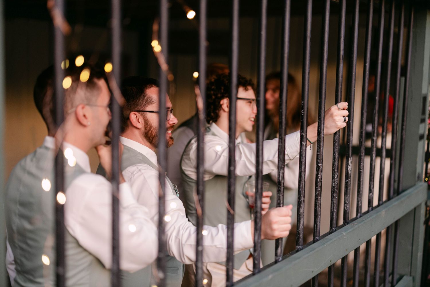 Wedding guests smiling and socializing behind decorative iron gate bars at an indoor reception venue.