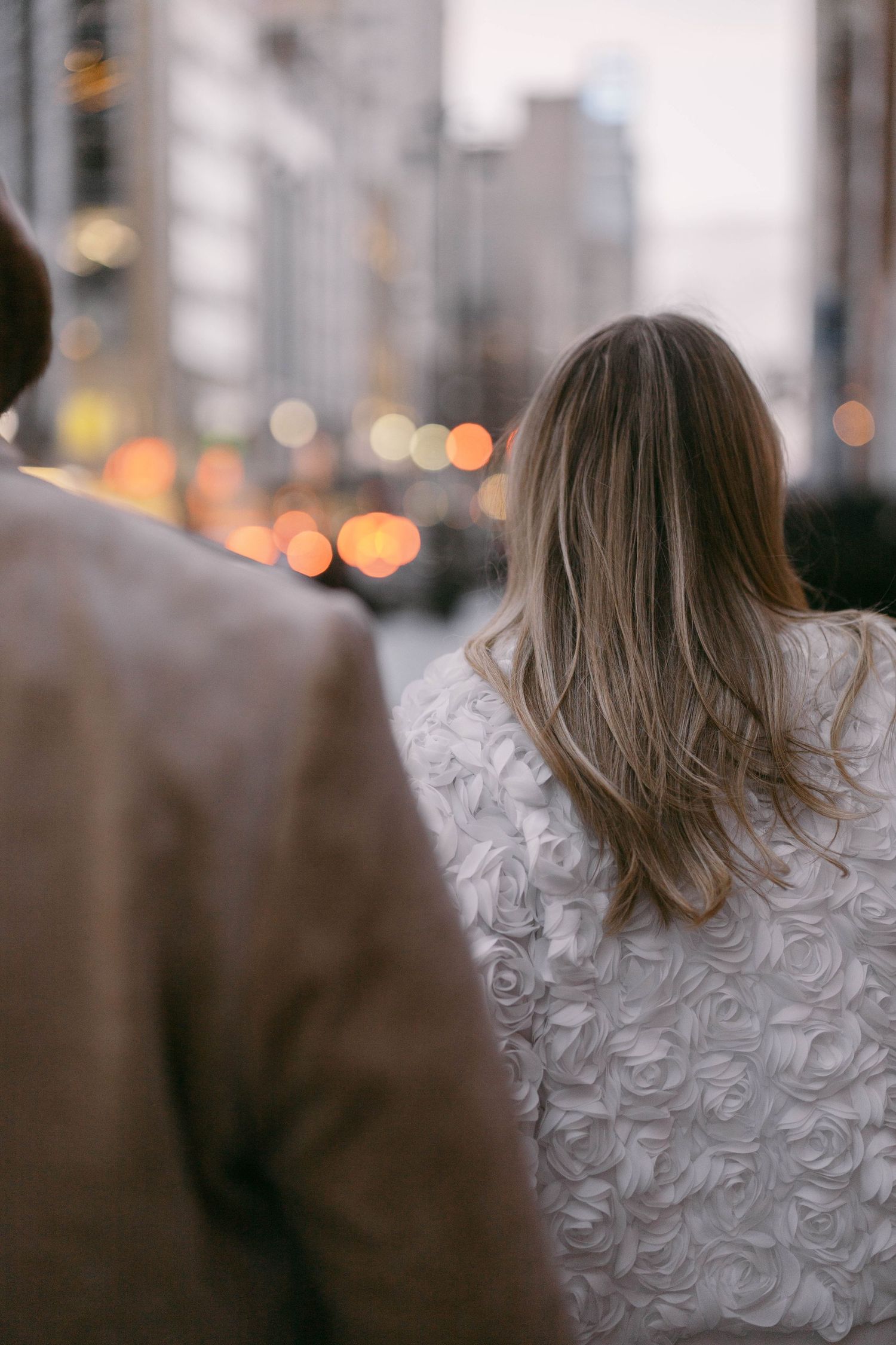Back view of textured white coat against blurred city lights at dusk.
