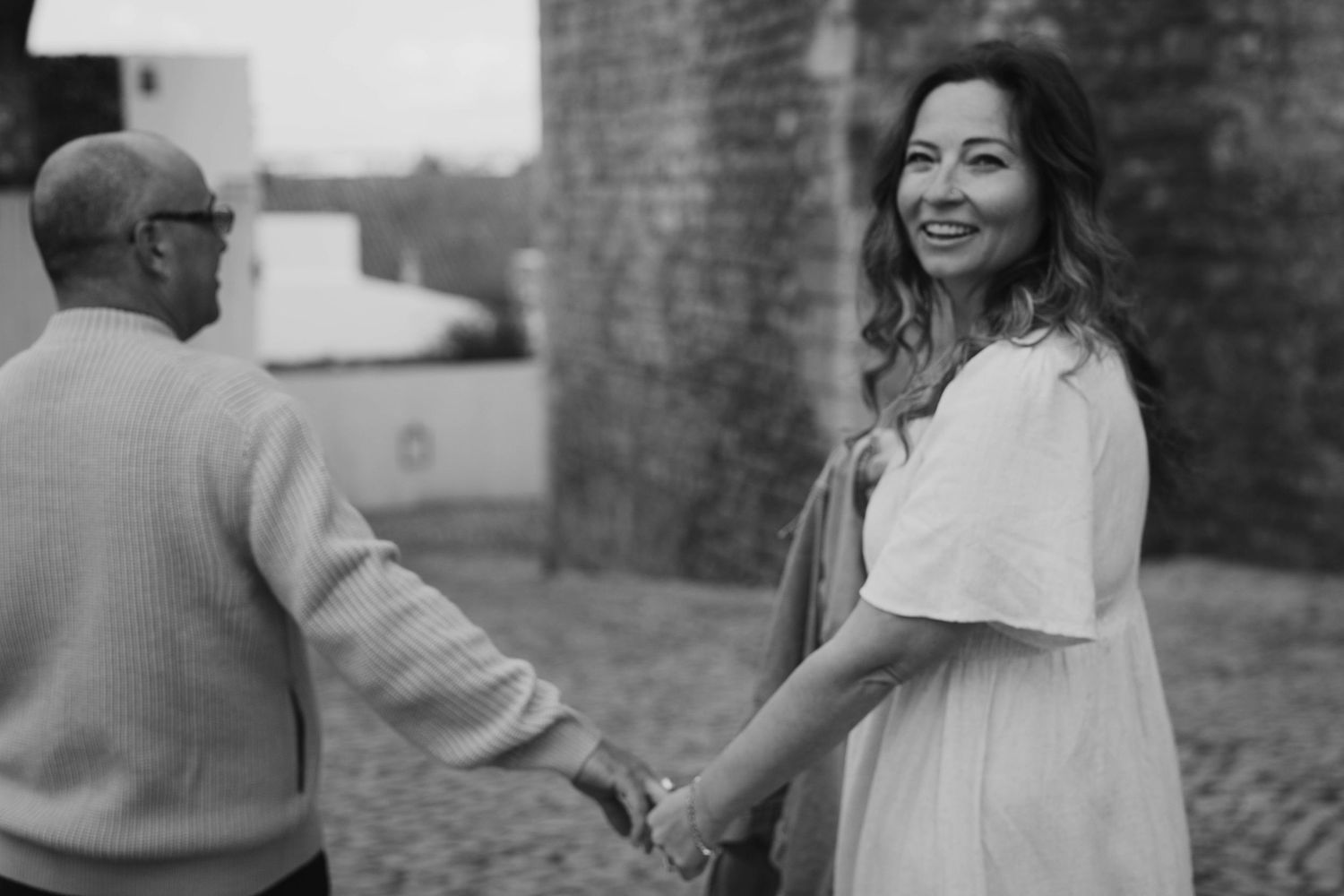 Black and white candid photo showing two people shaking hands and smiling at a brick building exterior.
