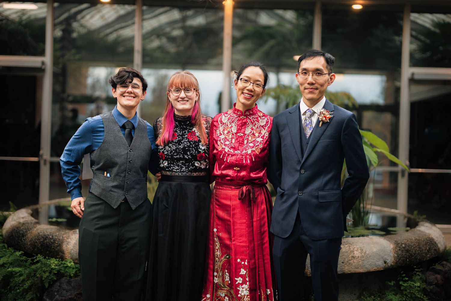 Four people smiling together at a wedding, one wearing a traditional red Chinese qipao dress in a greenhouse venue.