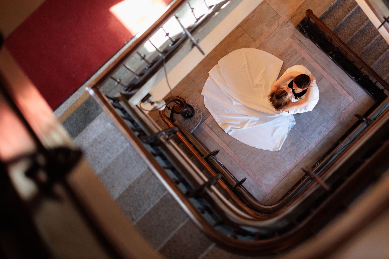 Aerial view of a bride in a white wedding gown standing at the bottom of an elegant staircase.