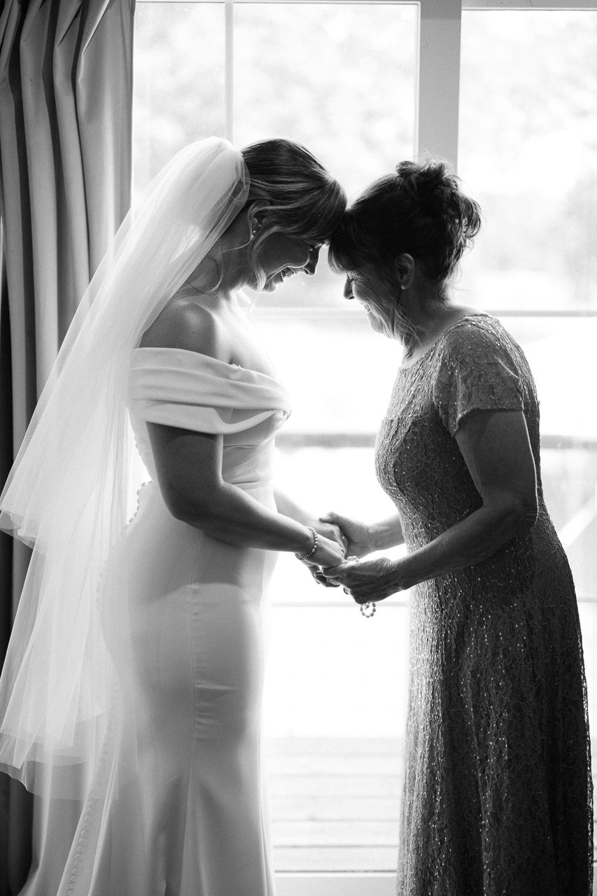 Black and white photo of a bride and her mother sharing a tender moment while holding hands before the wedding ceremony.