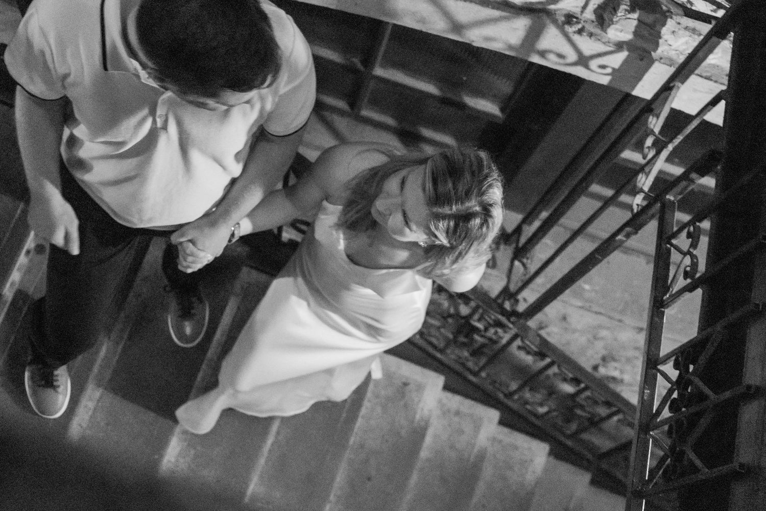 Black and white aerial view of a bride and groom holding hands while descending an elegant staircase.