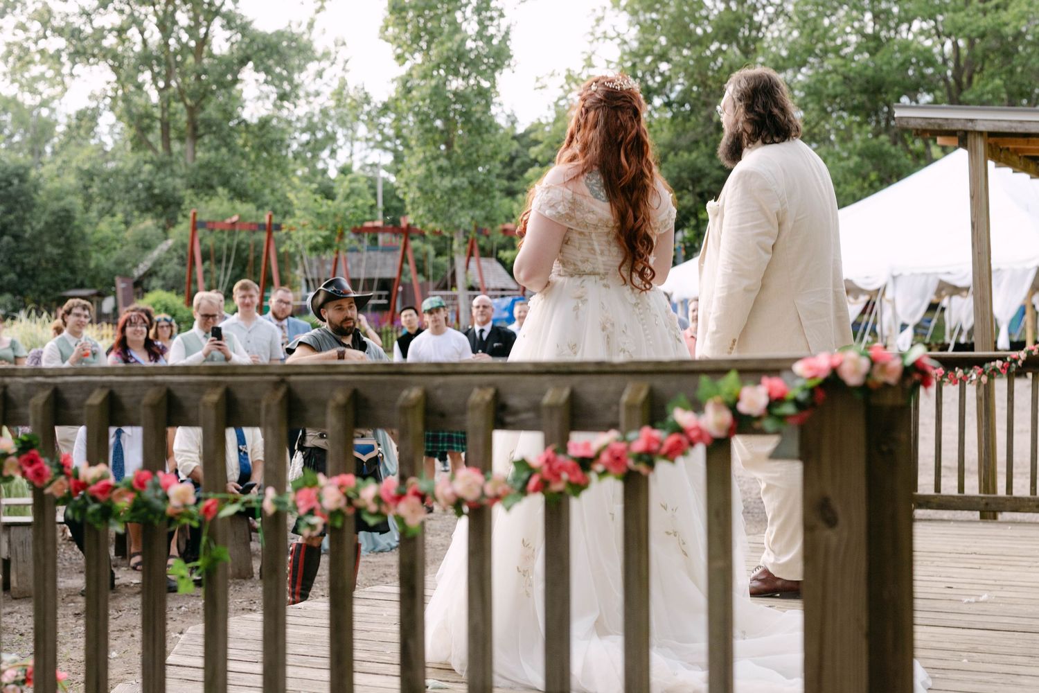 Bride and groom exchanging vows on a flower-decorated outdoor deck surrounded by guests.