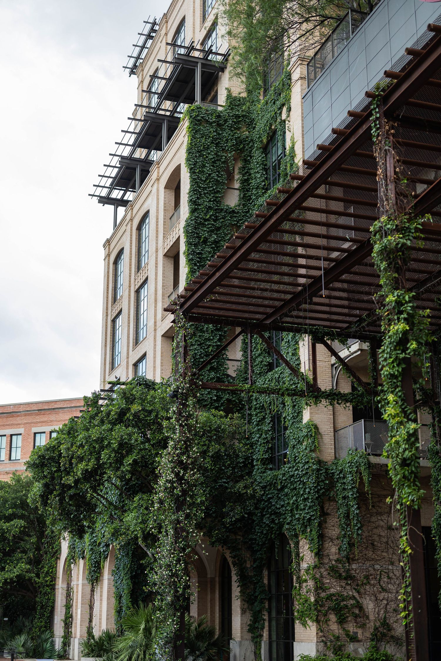 Ivy-covered building facade with metal pergola balconies and arched walkway in urban setting.