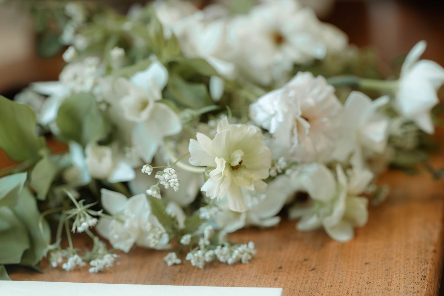 Delicate white and green floral arrangement with soft blooms and eucalyptus on a wooden surface.
