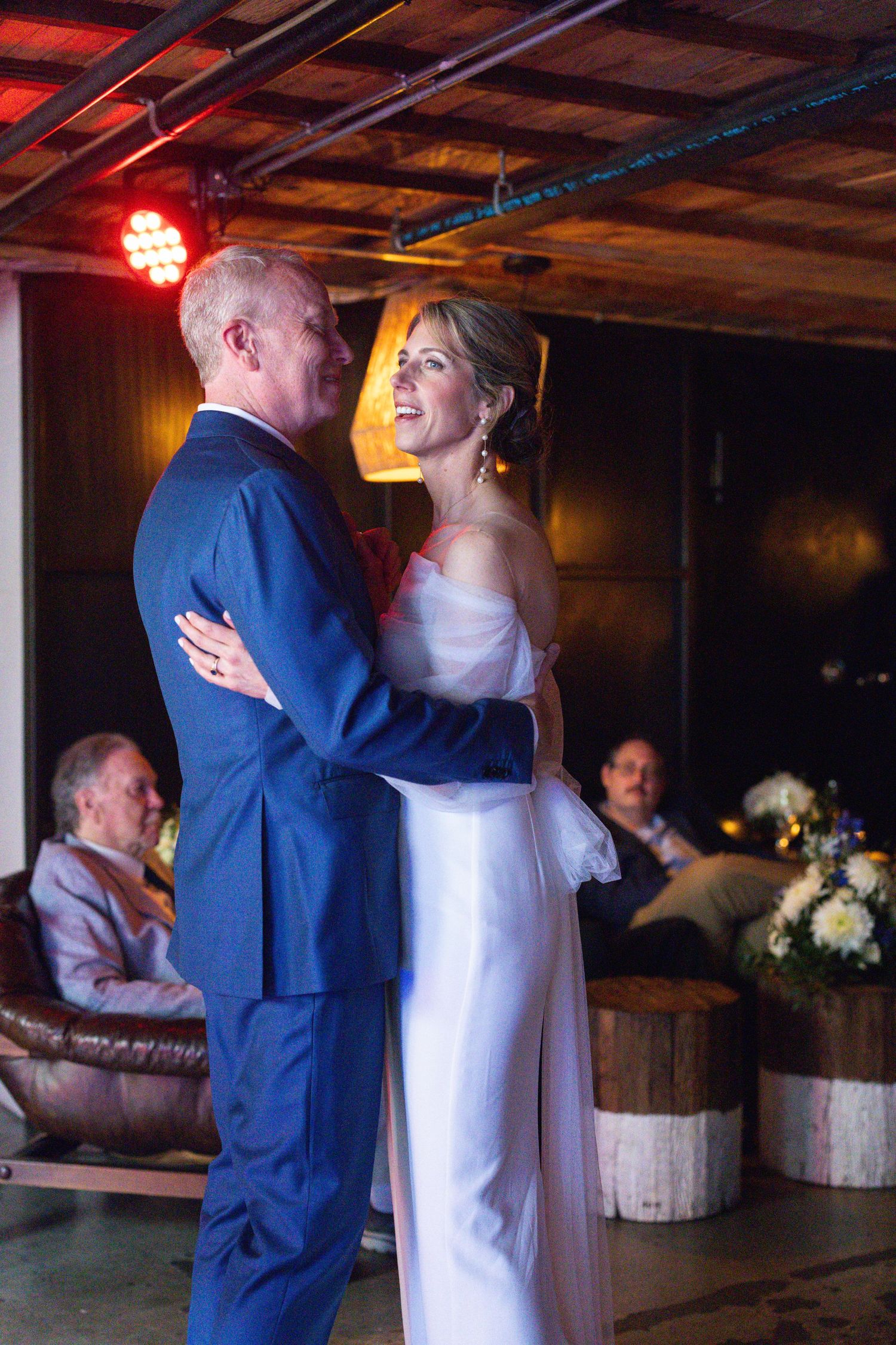A couple shares their first dance as newlyweds in a rustic barn venue with wooden decor and soft lighting.