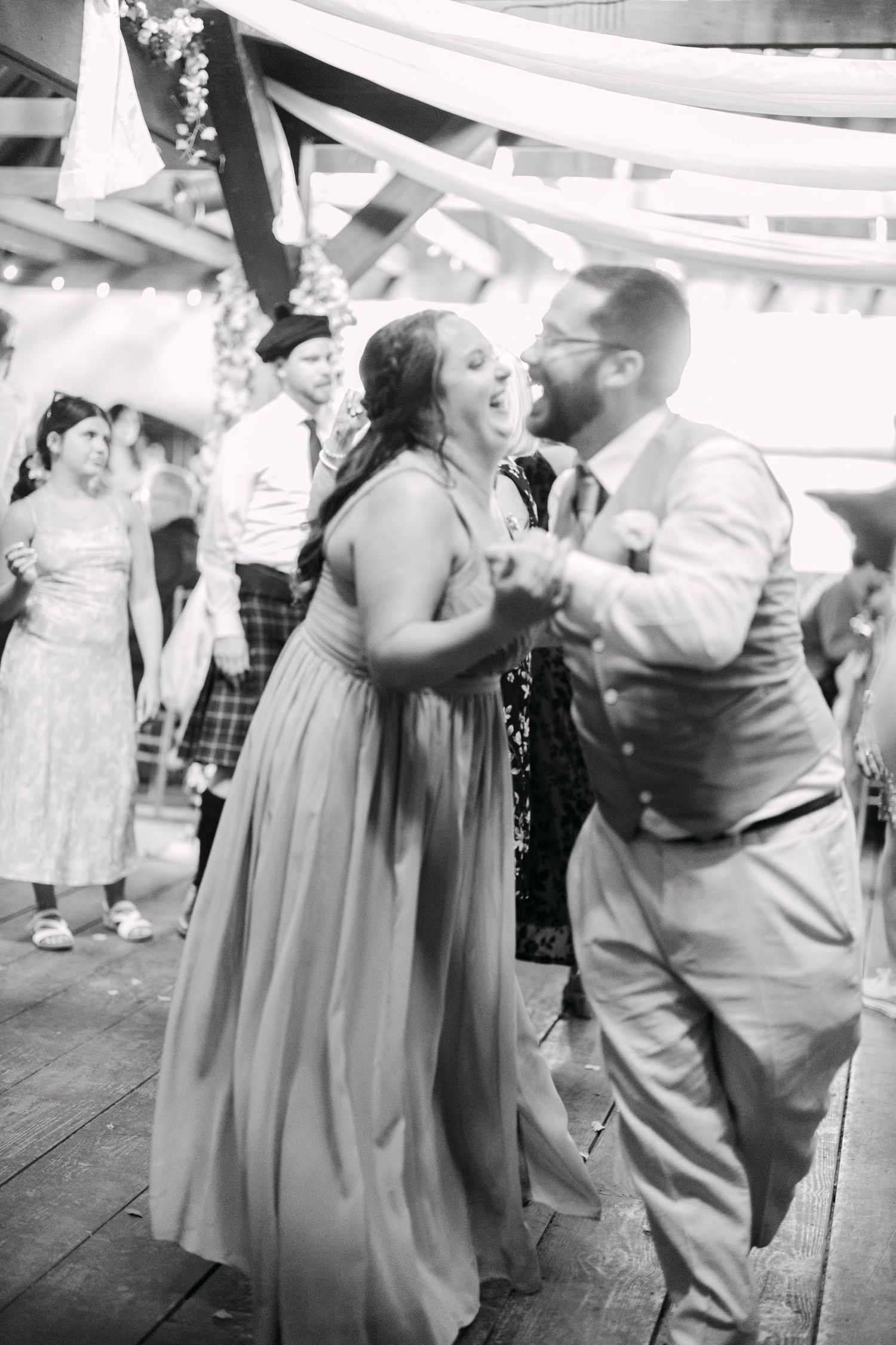 Bridesmaid and groomsman dance joyfully at a wedding reception in this black and white photo.