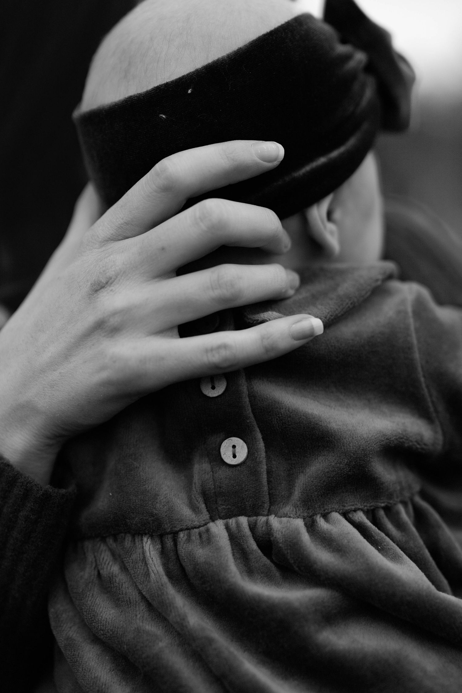Black and white photo of a person being blindfolded by another hand, wearing a buttoned jacket.