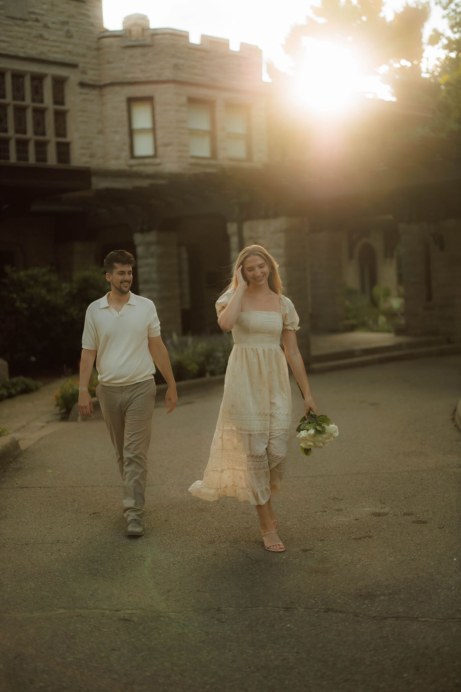 A couple walks together at sunset on a stone pathway near a building, creating a romantic silhouette against golden light.