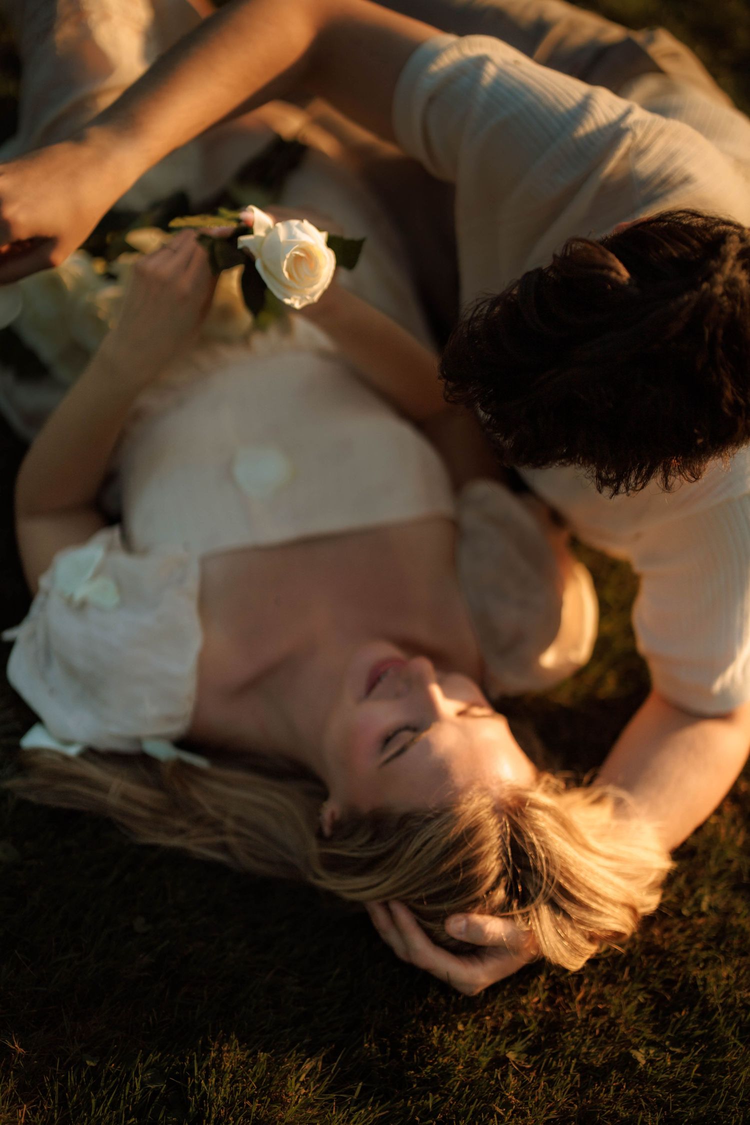 A dreamy sunset portrait of someone lying in grass wearing a white dress.