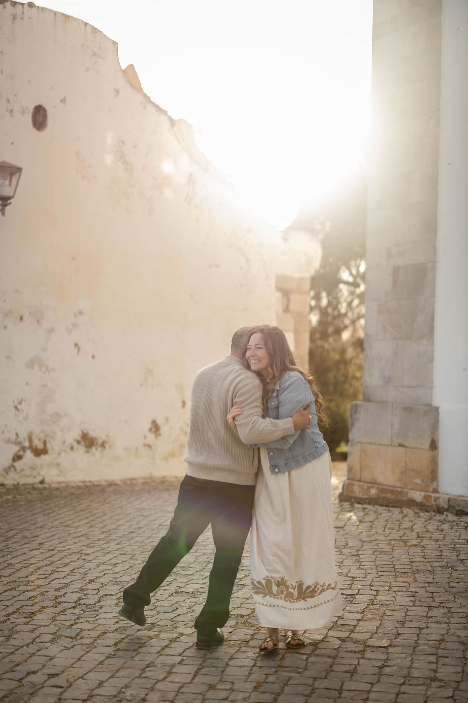 A romantic couple dancing on a cobblestone courtyard at sunset with warm golden light filtering through.