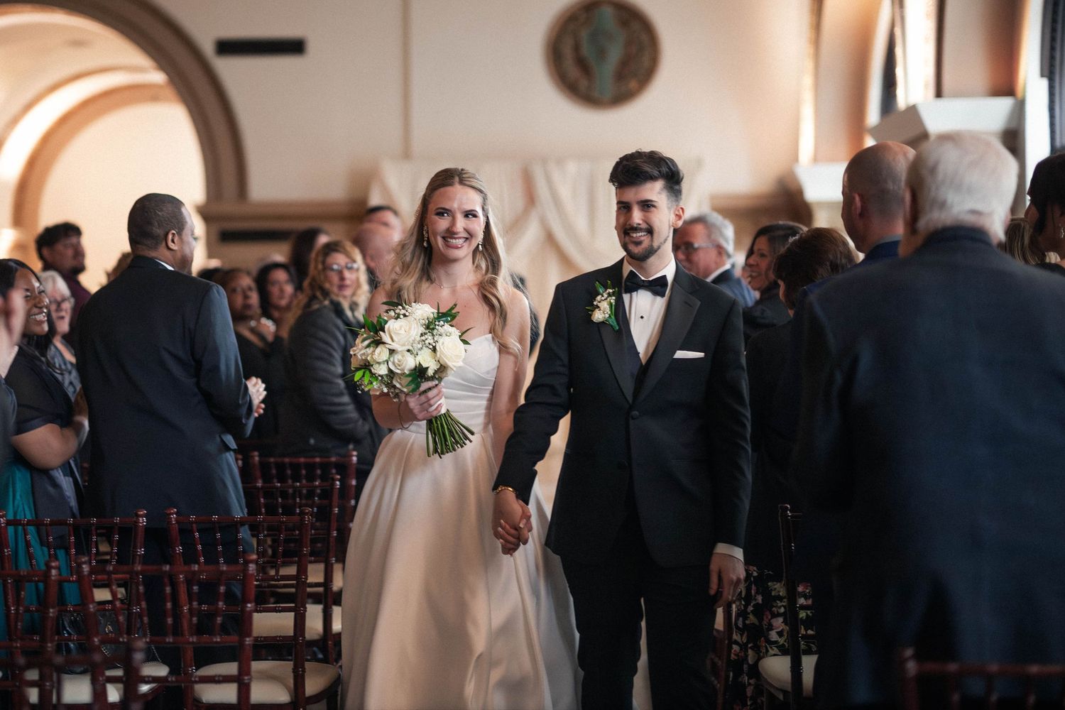 Bride and groom walk down the aisle hand in hand after wedding ceremony in elegant chapel.