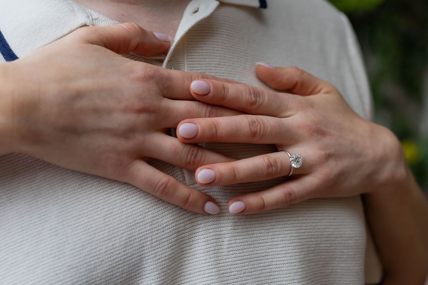 Close-up of two hands clasped together, one wearing a diamond solitaire engagement ring, symbolizing love and commitment.