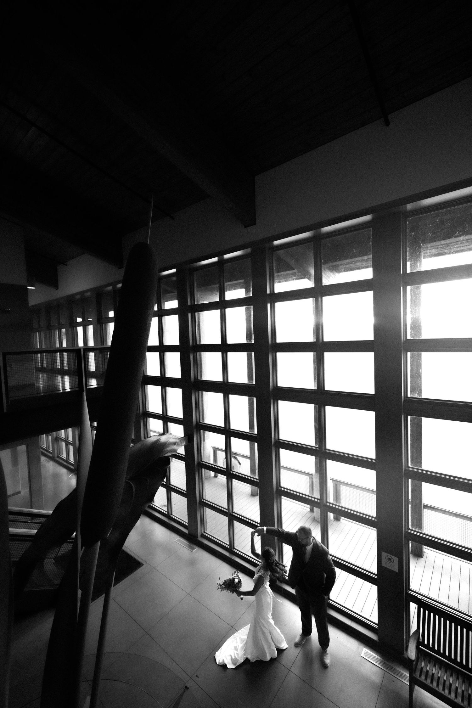 Silhouetted figures by large windows in a modern architectural space.