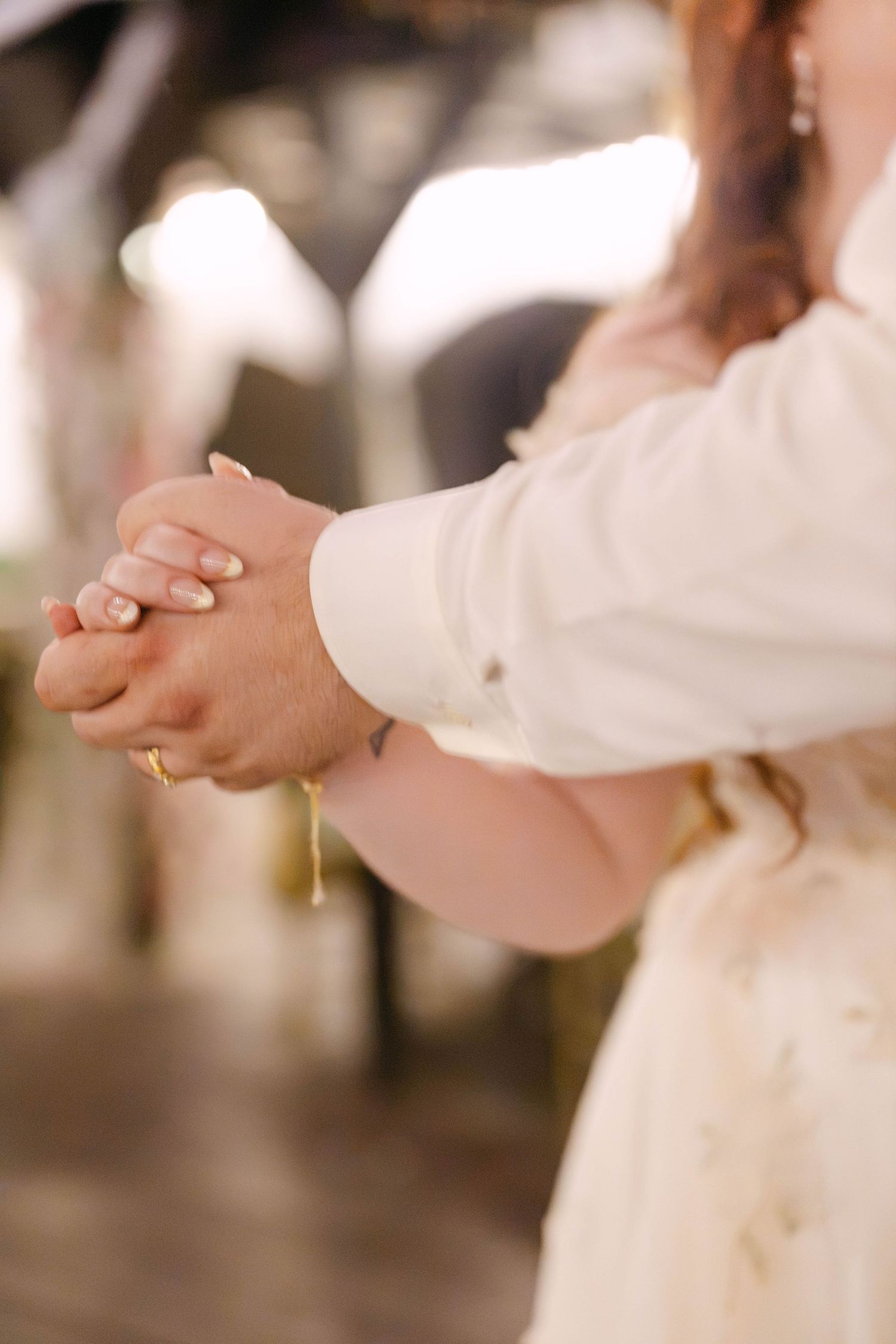 Bride and groom hold hands tenderly during their first dance at romantic wedding reception.
