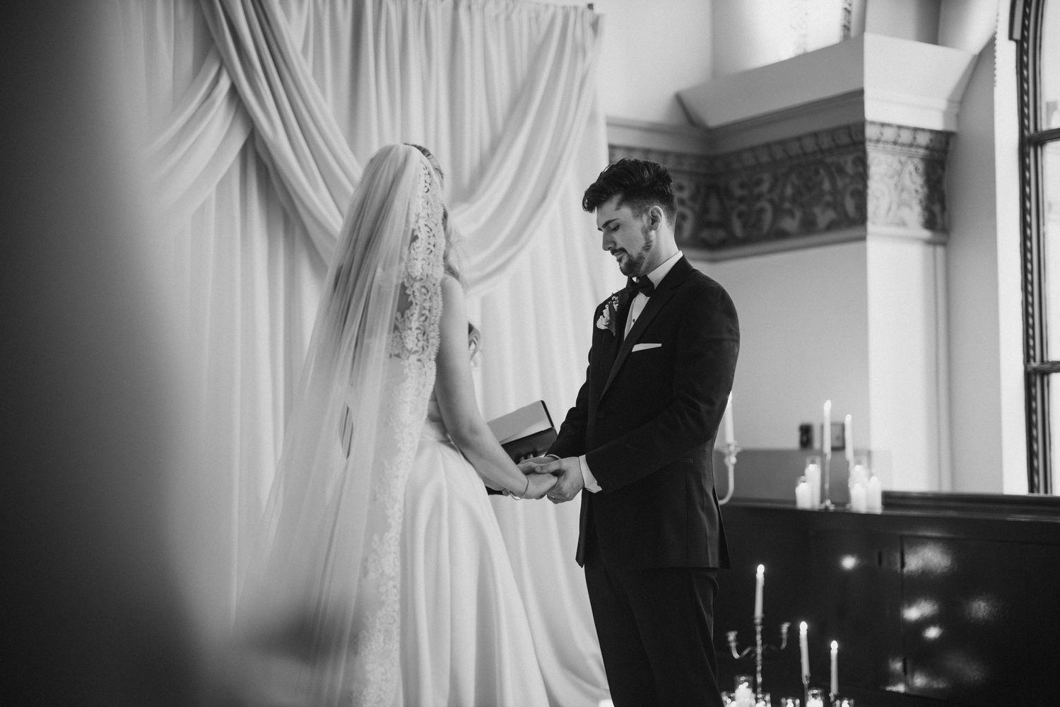 Black and white photo of bride and groom exchanging vows at elegant church wedding ceremony.