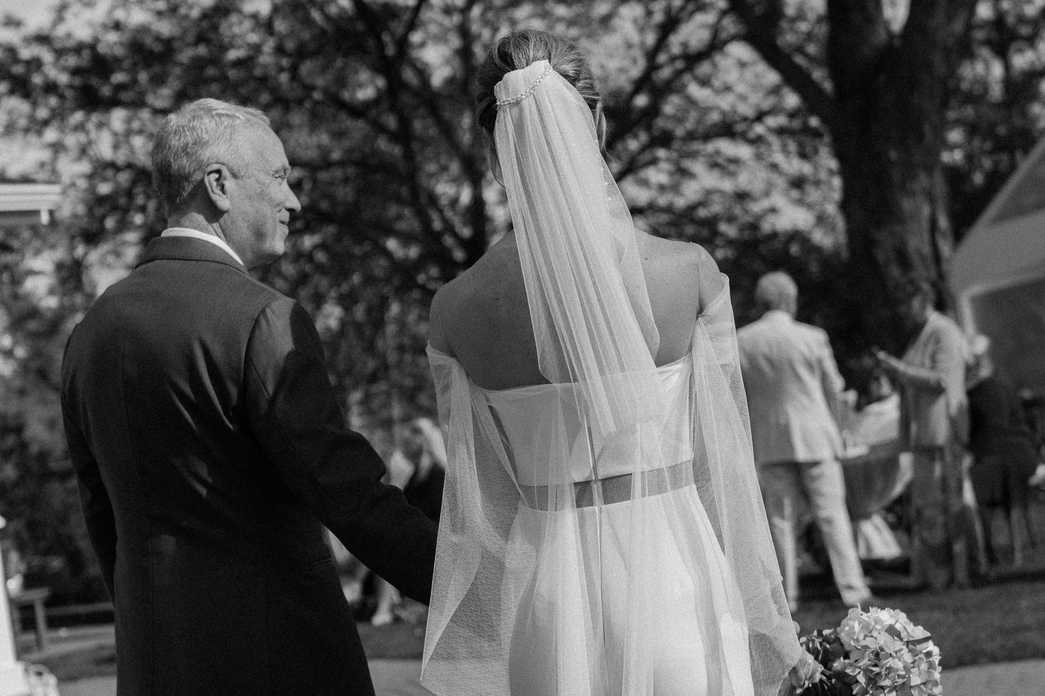 A wedding couple shares an intimate moment in a garden setting while surrounded by guests and natural scenery.