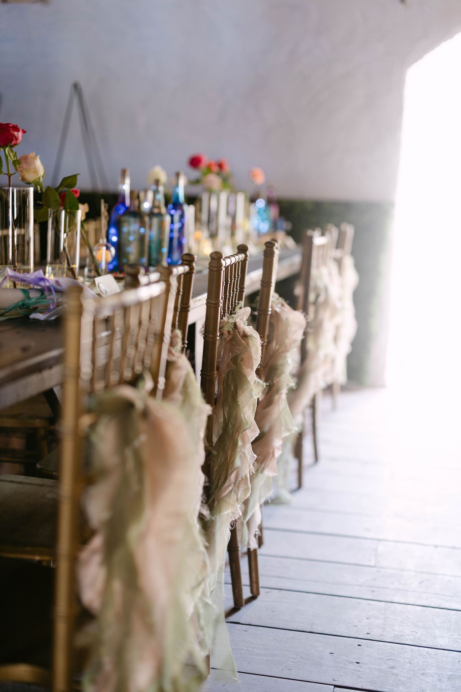 Elegant gold chiavari chairs with ruffled fabric sashes line a rustic wooden reception dinner table.