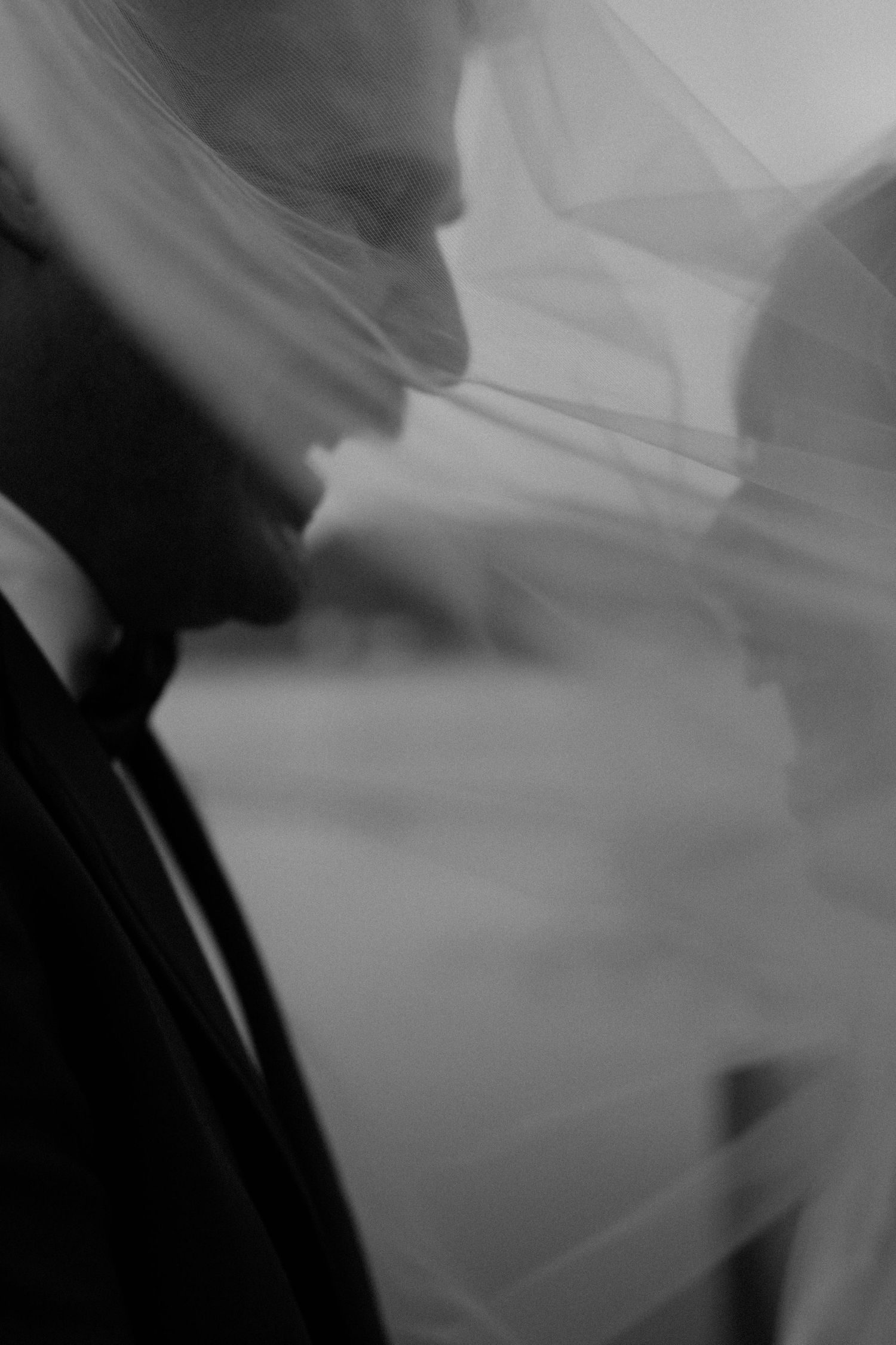 Black and white artistic wedding photo of bride and groom sharing an intimate moment beneath a flowing veil.