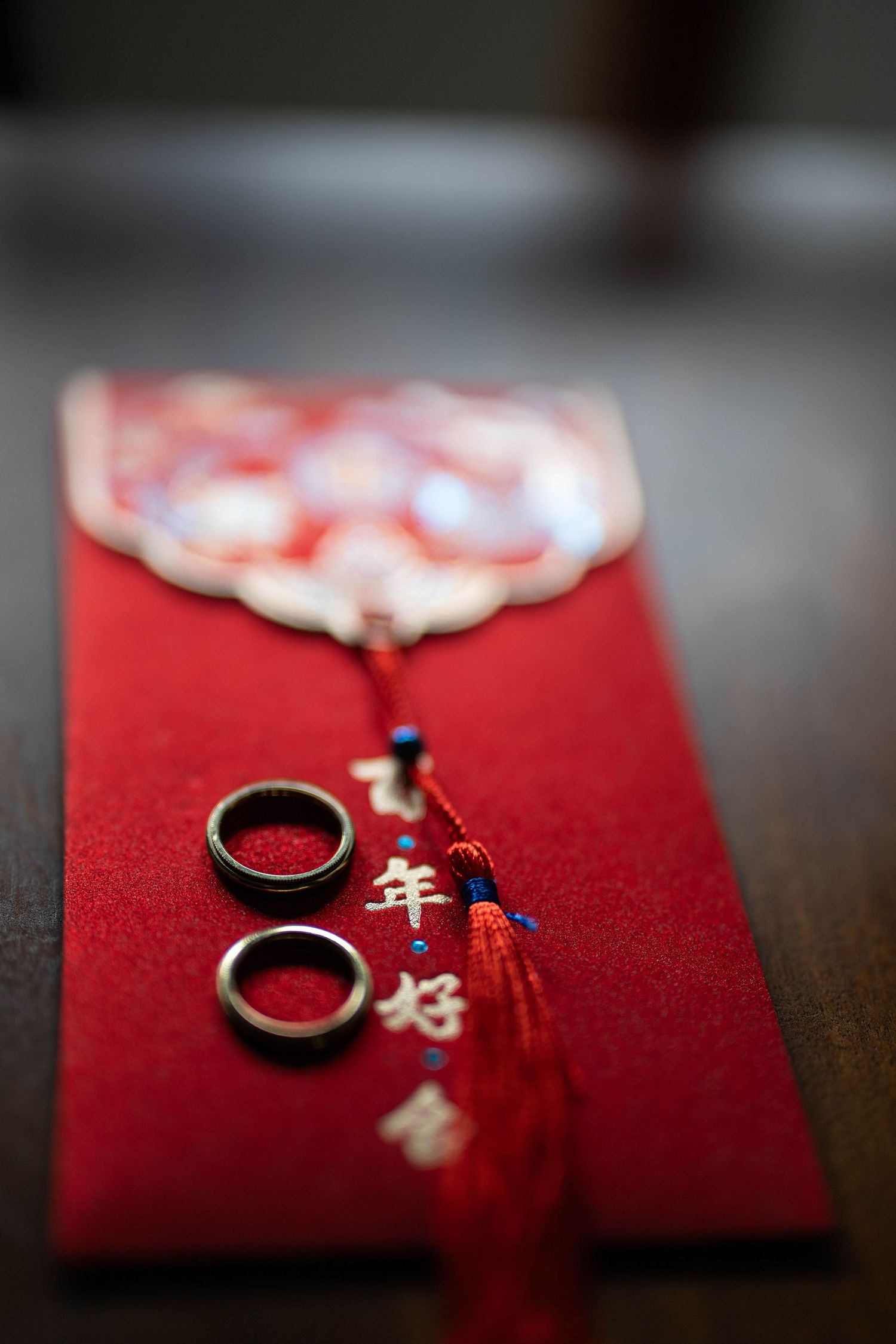 Two gold wedding rings rest on a red Chinese lucky envelope with gold characters and decorative tassel.