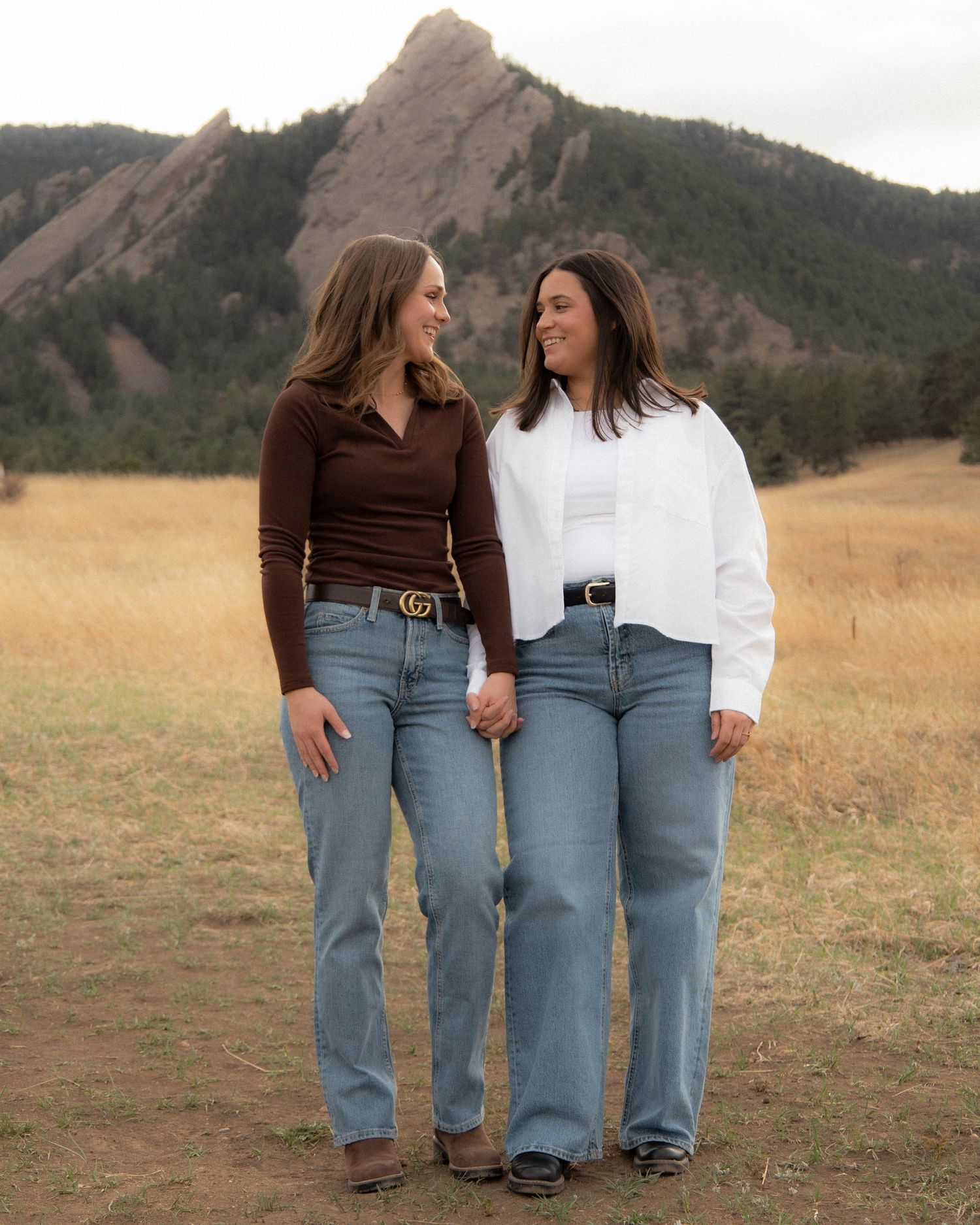 two women holding hands posing in front of the flat irons in a yellow field in Boulder, Colorado