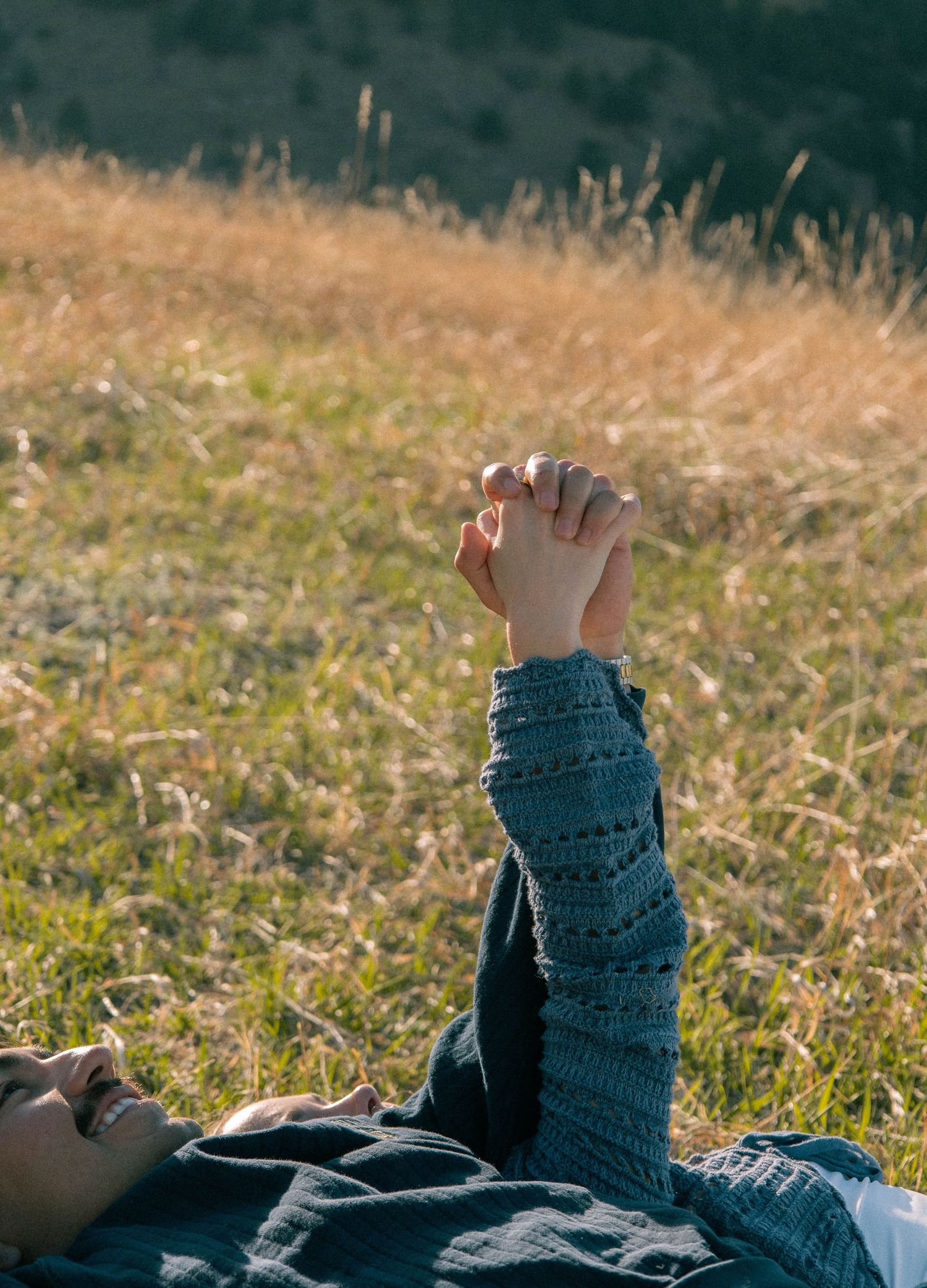 A couple lying in the grass holding hands raised towards the sky in a grassy field in Boulder, Colorado