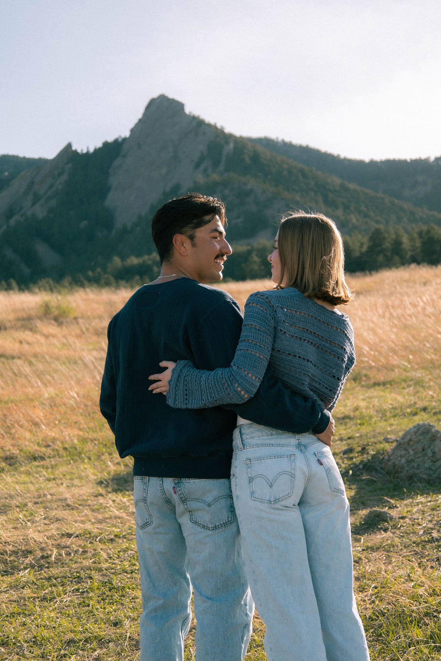 A couple facing away from the camera with arms wrapped around each other smiling and looking at each other in Boulder, Colorado