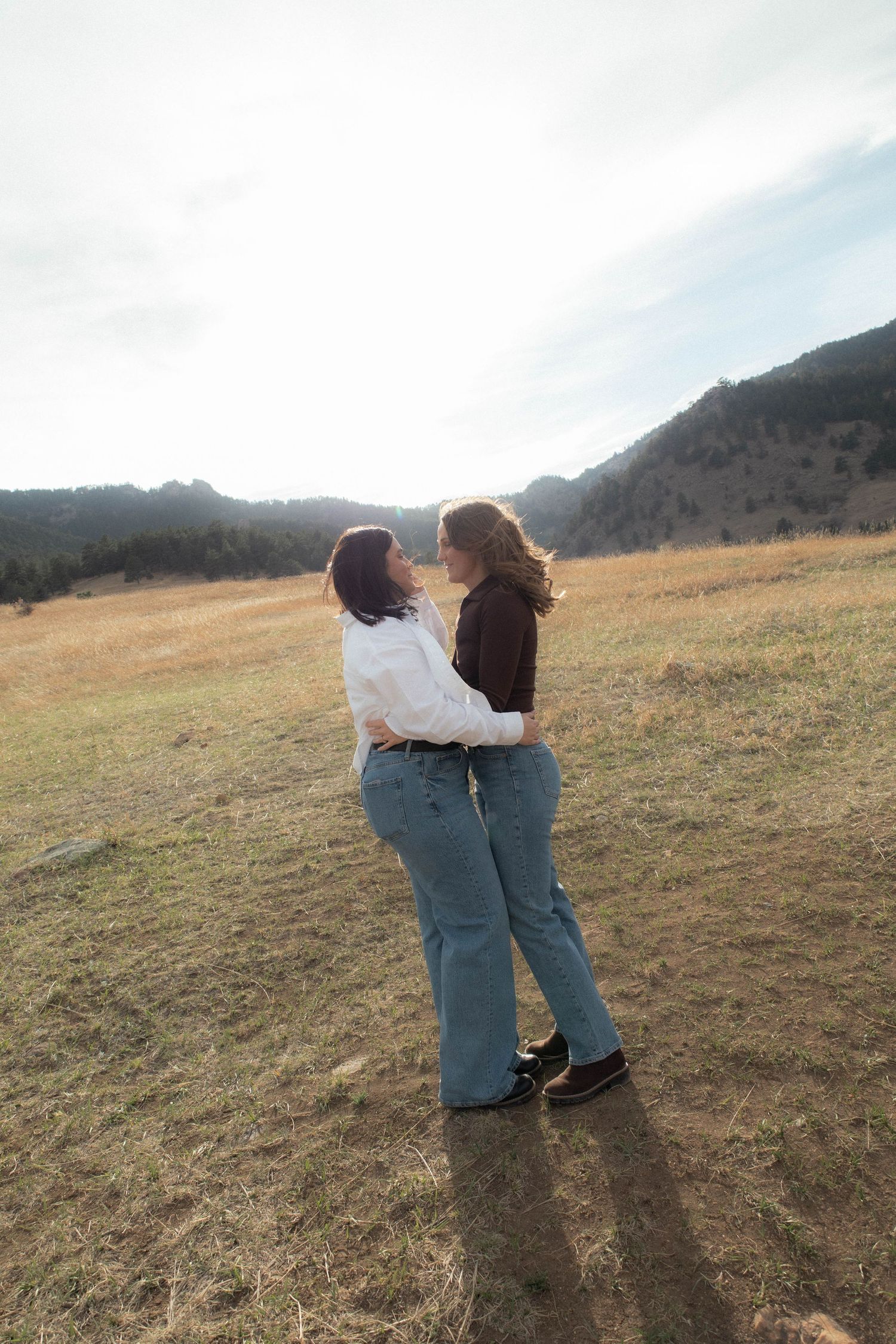 a couple standing with arms wrapped around one another in a green field with the sun behind them in Boulder, Colorado