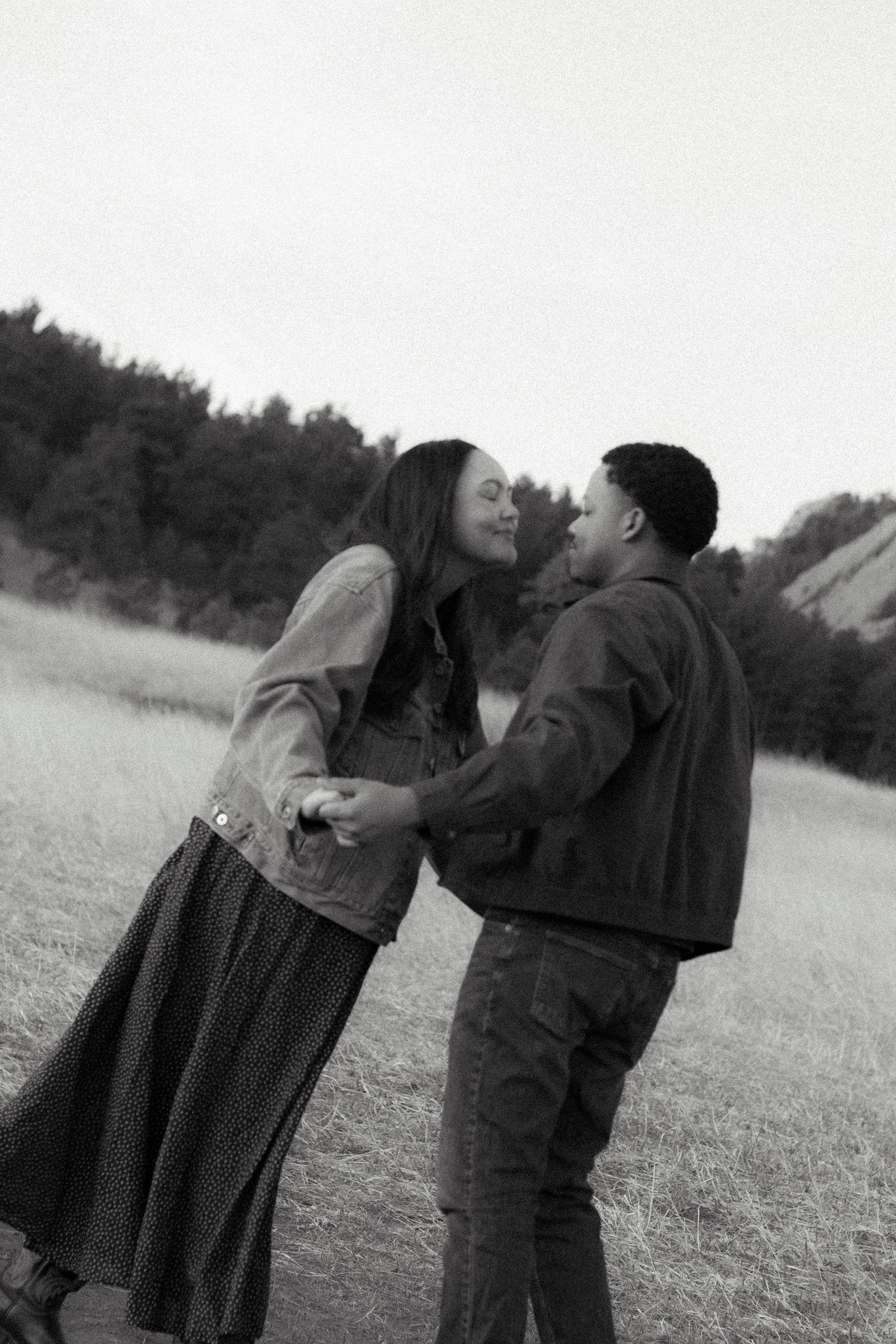 A black and white photo of a couple holding hands and leaning into kiss in Boulder, Colorado