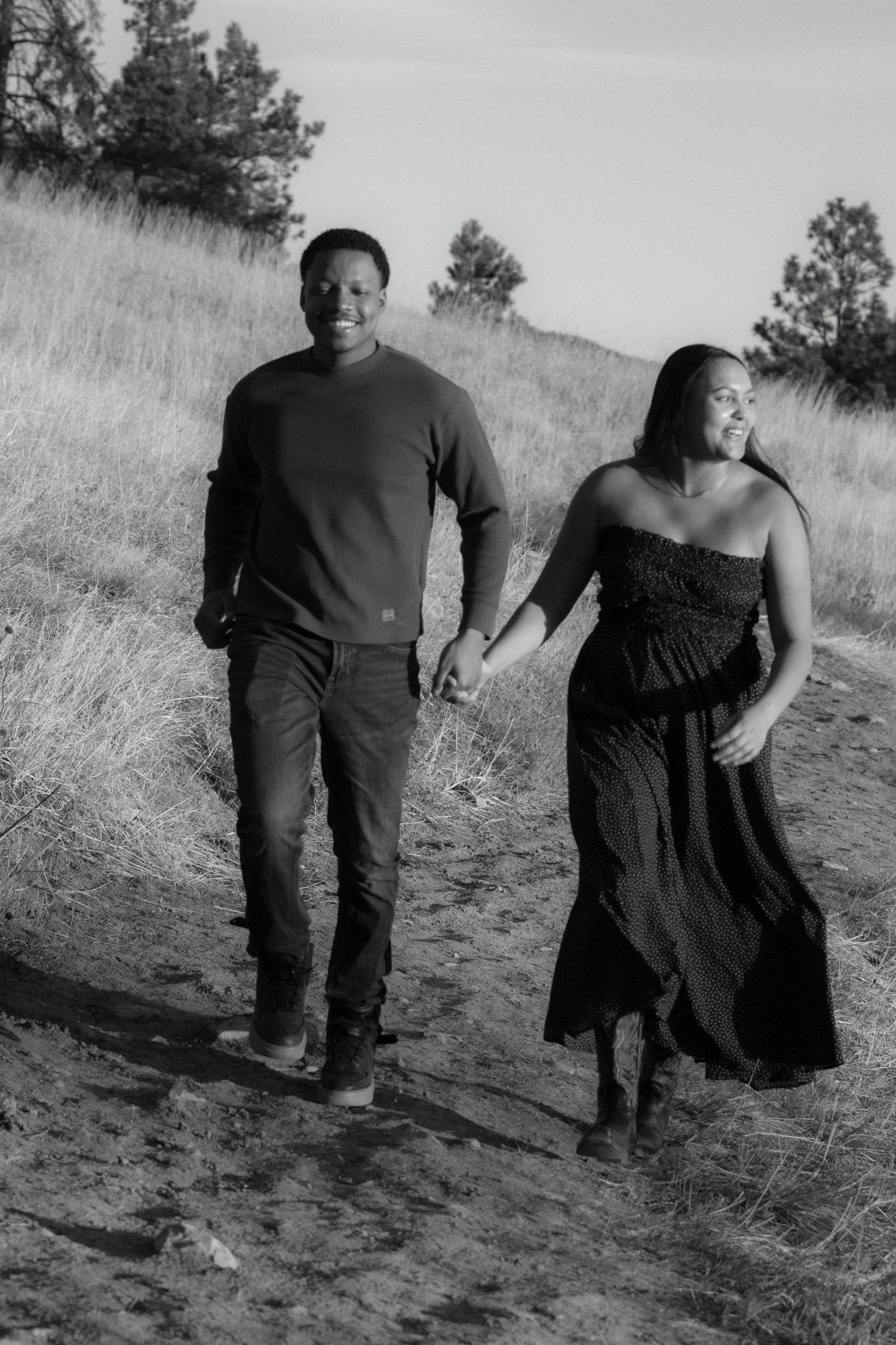 a black and white photo of a couple holding hands and running on a dirt trail in Boulder, Colorado
