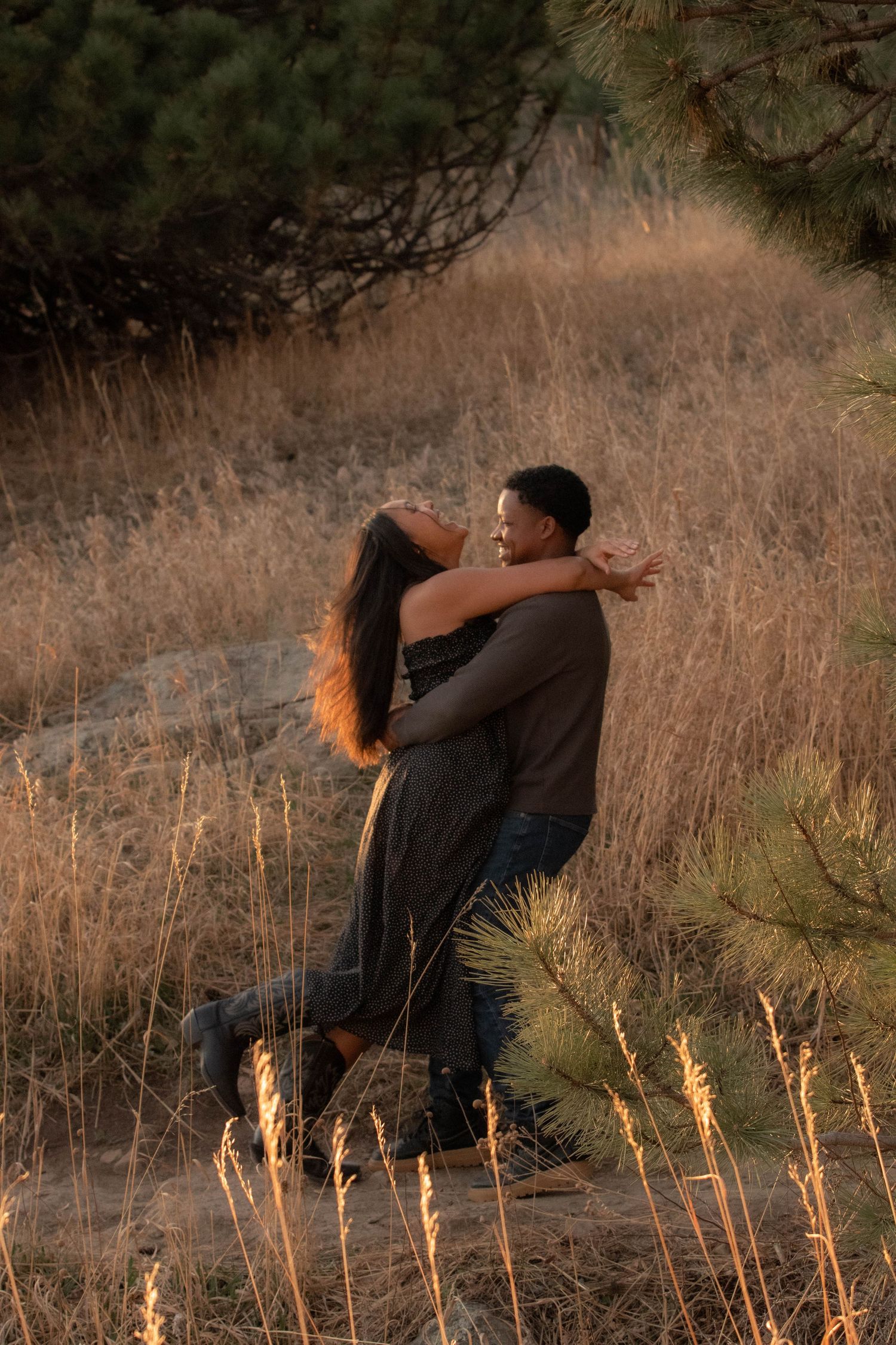 A couple spinning in a grass field with golden light shining on them laughing in Boulder, Colorado