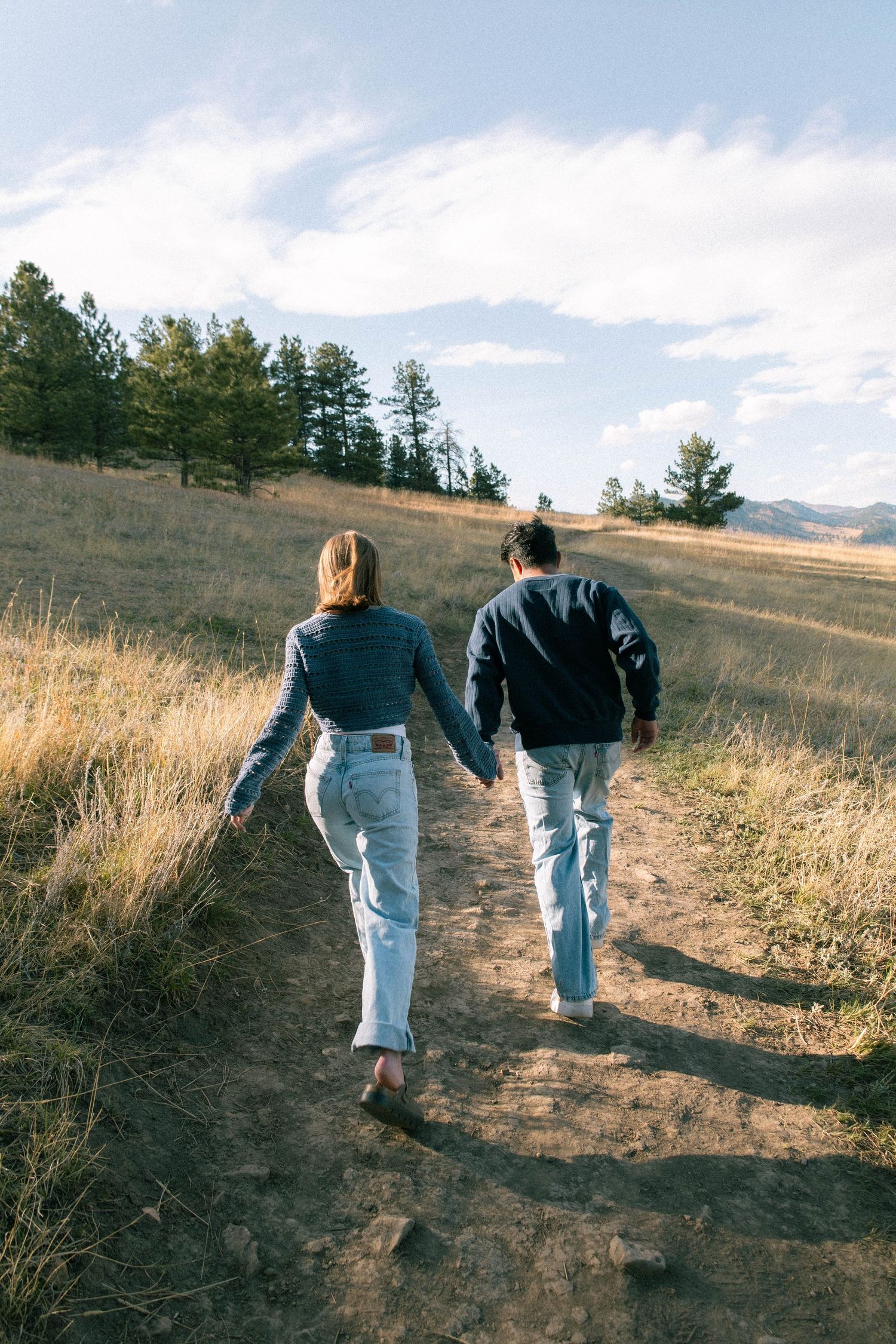 A couple holding hands and running away from the camera on a dirt path in Boulder, Colorado