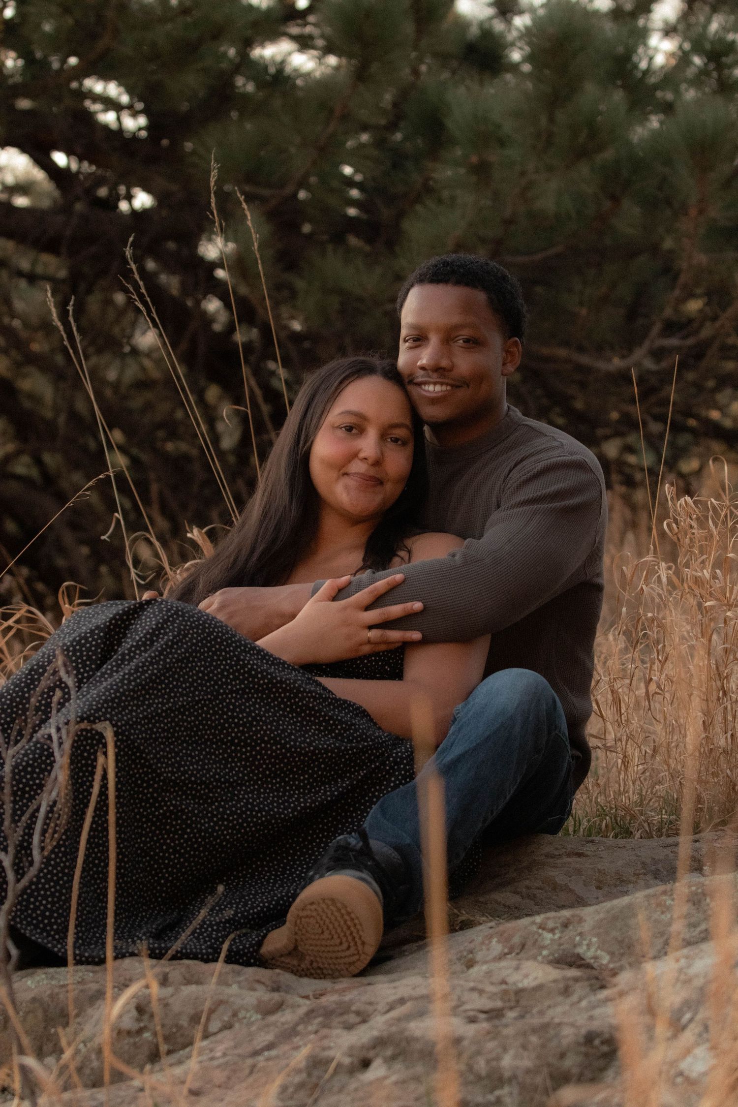a couple sitting on a rock smiling at the camera with greenery behind them in Boulder, Colorado